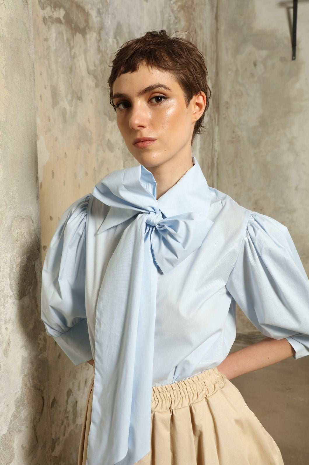 Model wearing the Karin Sky Blue Short Sleeves Blouse by House of Nomad Stories, featuring organic cotton fabric, sculptural balloon sleeves, structured silhouette, and a versatile neck tie detail.