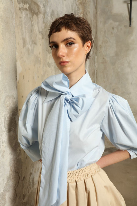 Model wearing the Karin Sky Blue Short Sleeves Blouse by House of Nomad Stories, featuring organic cotton fabric, sculptural balloon sleeves, structured silhouette, and a versatile neck tie detail.