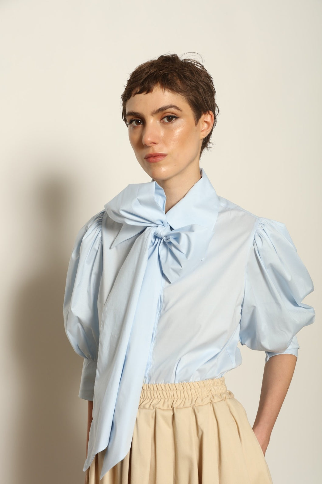 Model wearing the Karin Sky Blue Short Sleeves Blouse by House of Nomad Stories, featuring organic cotton fabric, sculptural balloon sleeves, structured silhouette, and a versatile neck tie detail.