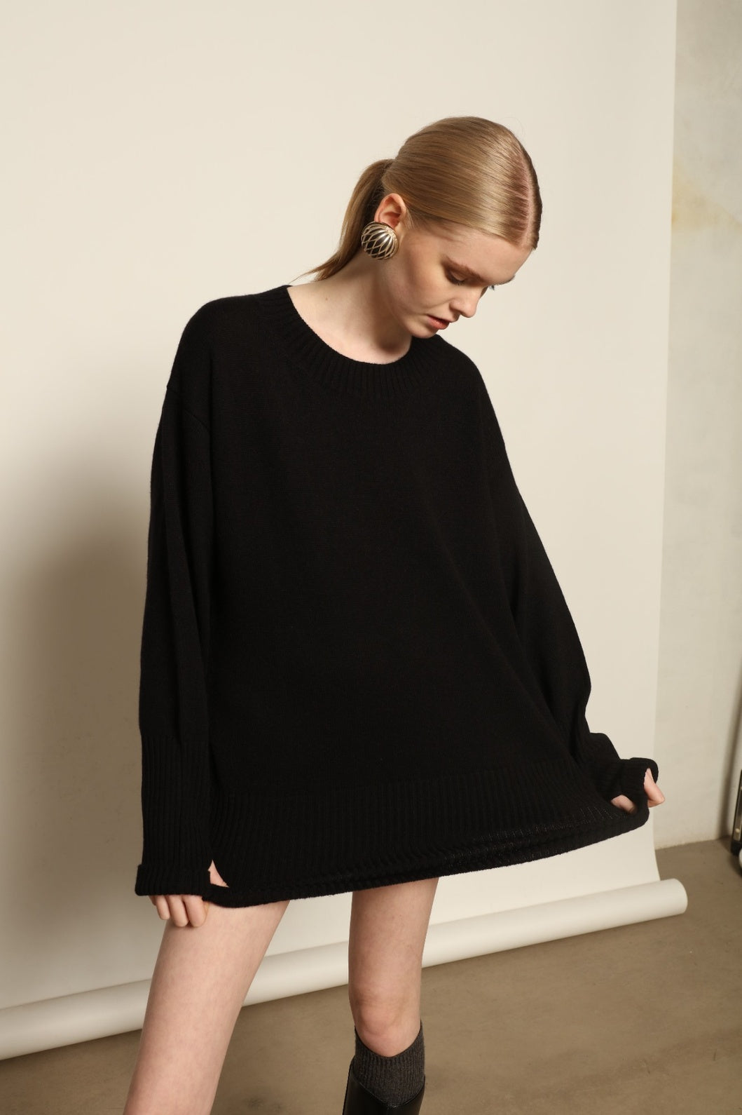 Model is wearing the Black Noemi Round Neck Long Sweater by House of Woven Stories, a pure ethically sourced cashmere knit in deep black with long silhouette, round neckline and ribbed edges.