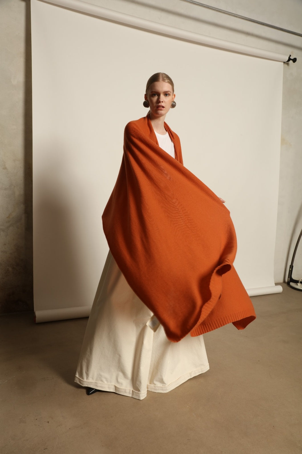 Model is wearing the Brick Leni Scarf by House of Woven Stories, a pure ethically sourced cashmere scarf with refined texture, enduring softness and fluid drape in a warm brick tone.