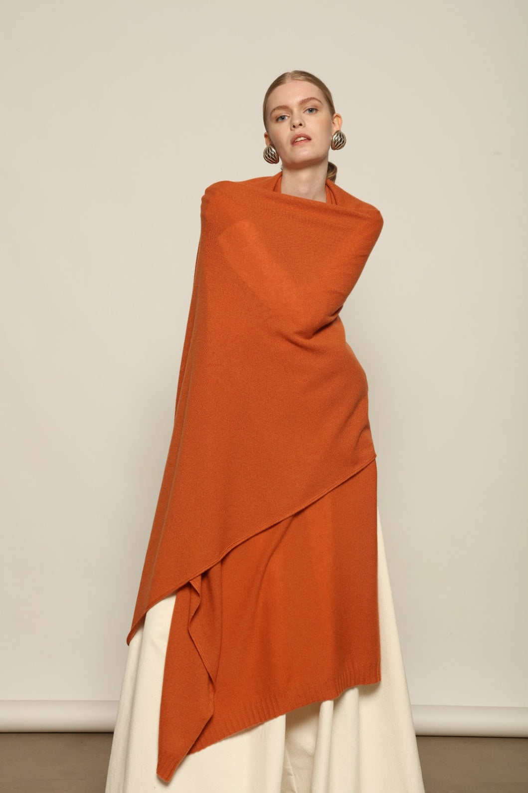 Model is wearing the Brick Leni Scarf by House of Woven Stories, a pure ethically sourced cashmere scarf with refined texture, enduring softness and fluid drape in a warm brick tone.