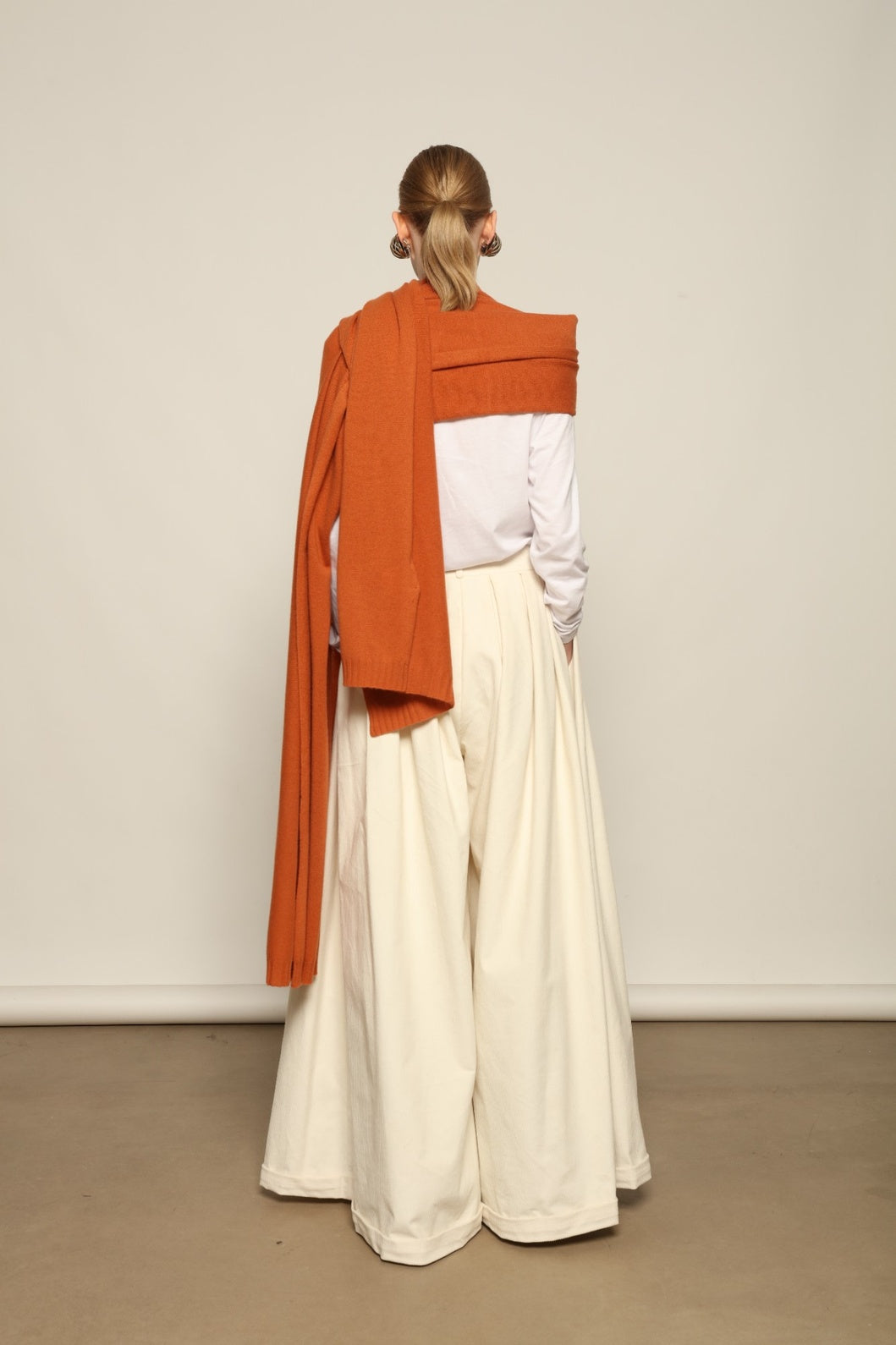 Model is wearing the Brick Leni Scarf by House of Woven Stories, a pure ethically sourced cashmere scarf with refined texture, enduring softness and fluid drape in a warm brick tone.