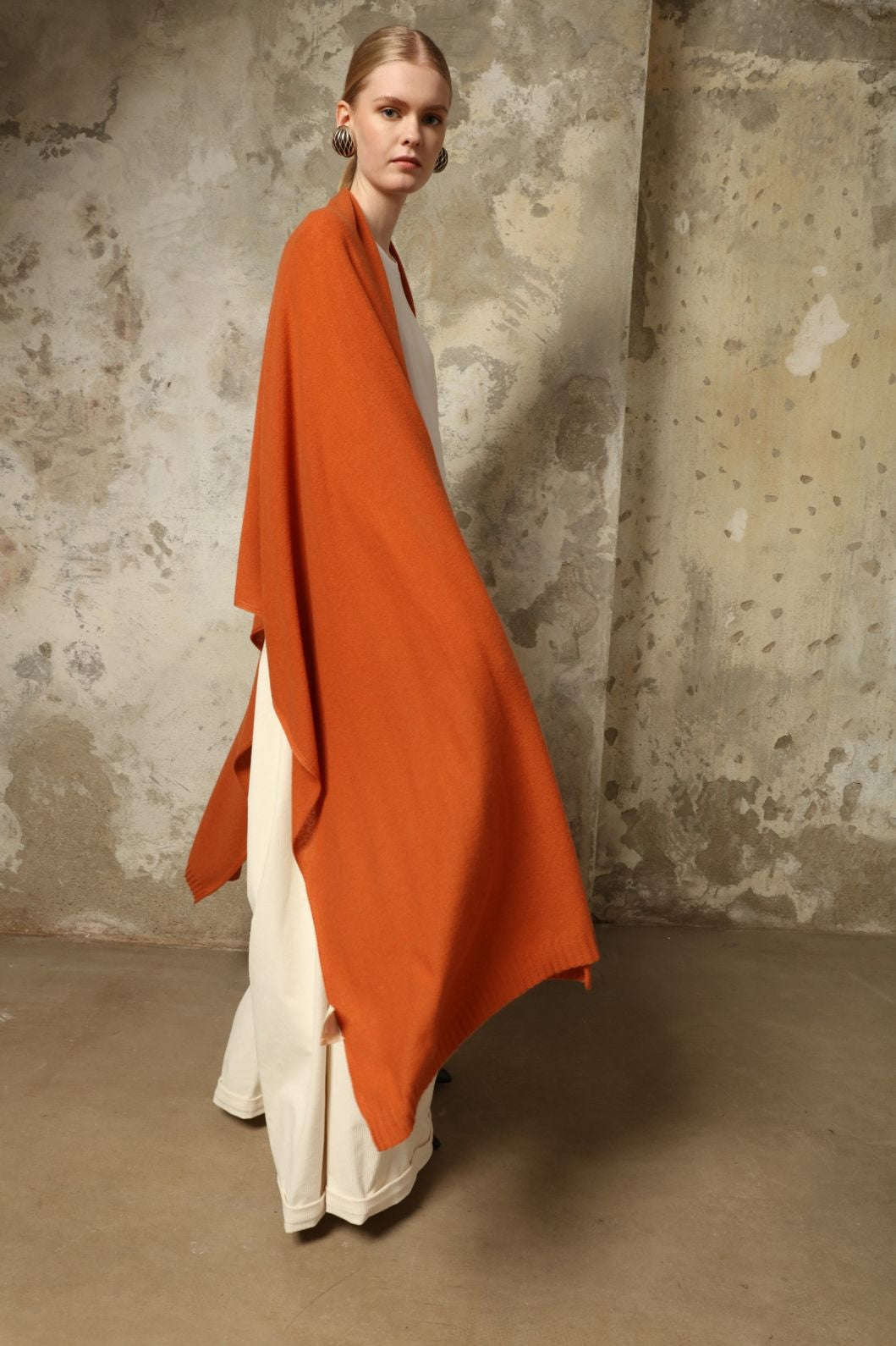 Model is wearing the Brick Leni Scarf by House of Woven Stories, a pure ethically sourced cashmere scarf with refined texture, enduring softness and fluid drape in a warm brick tone.