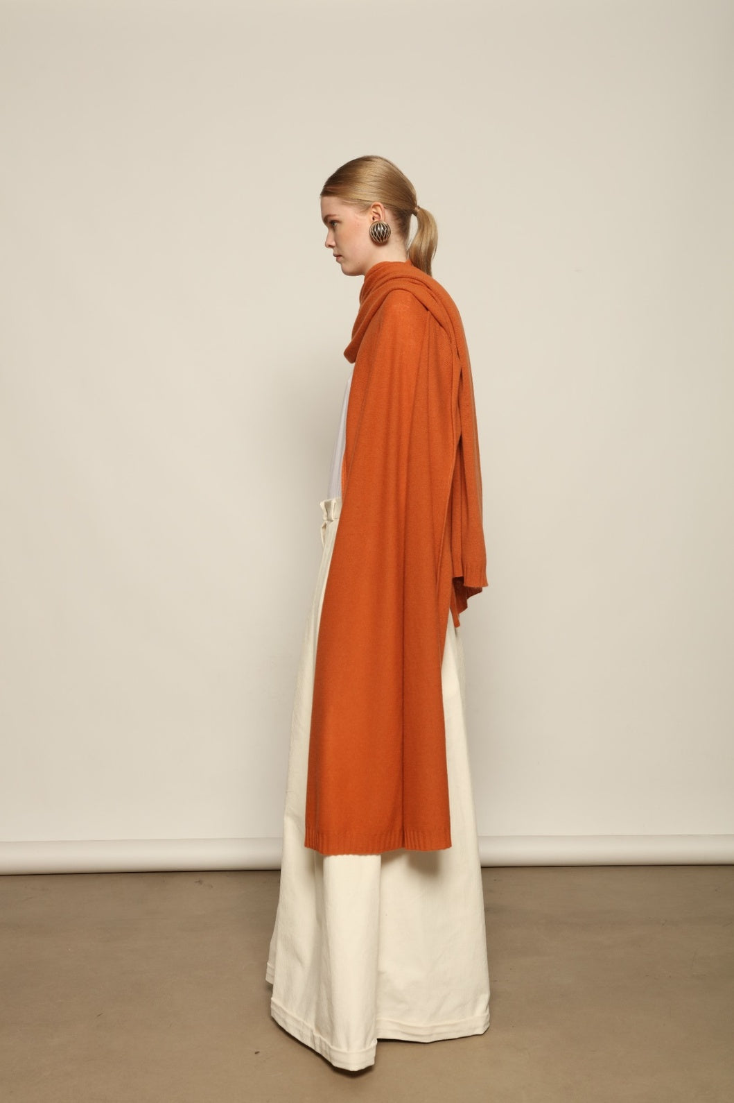 Model is wearing the Brick Leni Scarf by House of Woven Stories, a pure ethically sourced cashmere scarf with refined texture, enduring softness and fluid drape in a warm brick tone.