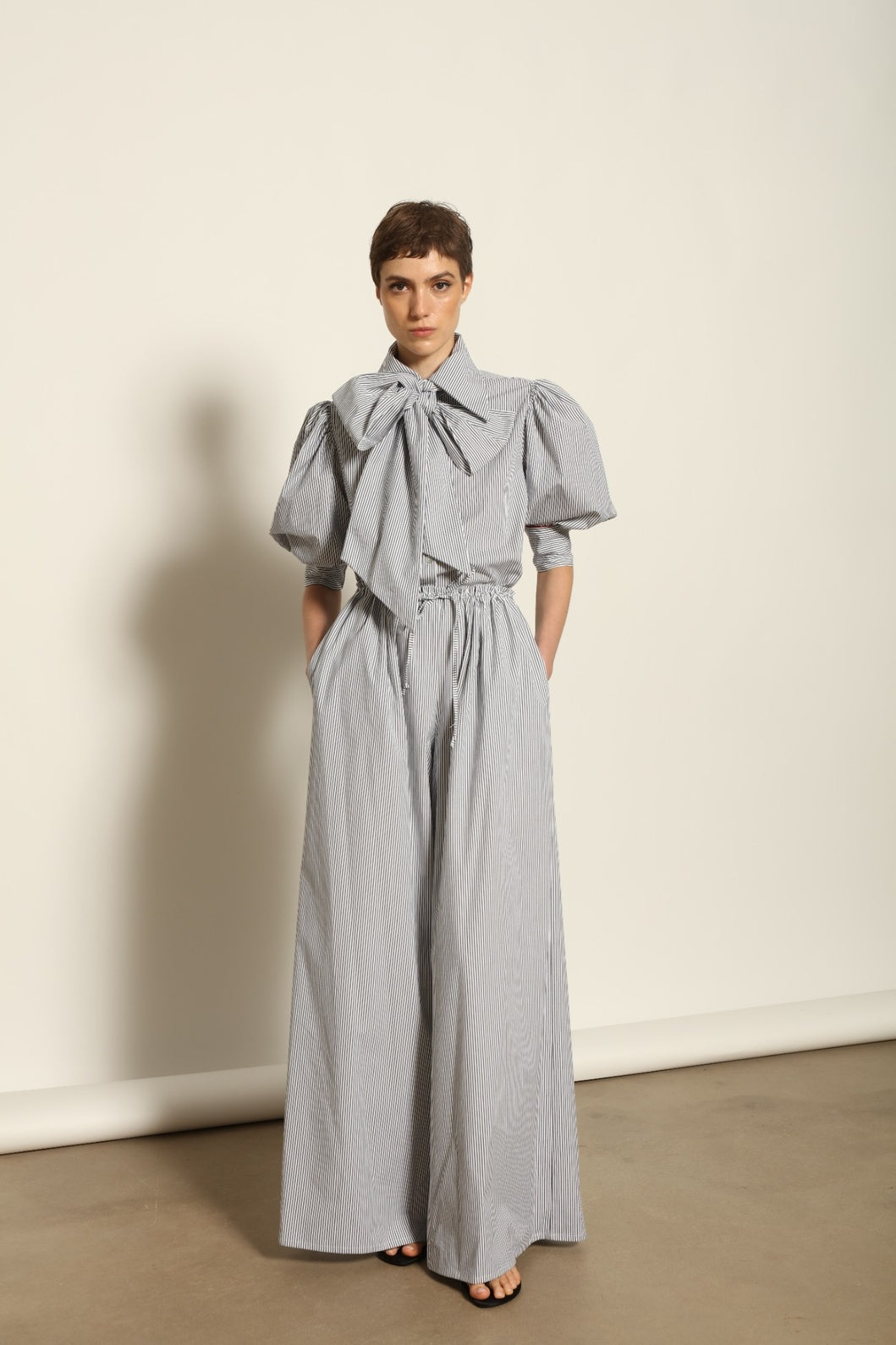 Model wearing the Brigitta White Navy Striped Trousers by House of Woven Stories, featuring 100% organic cotton fabric, high-rise waist, wide-leg silhouette, and classic white and navy stripes.