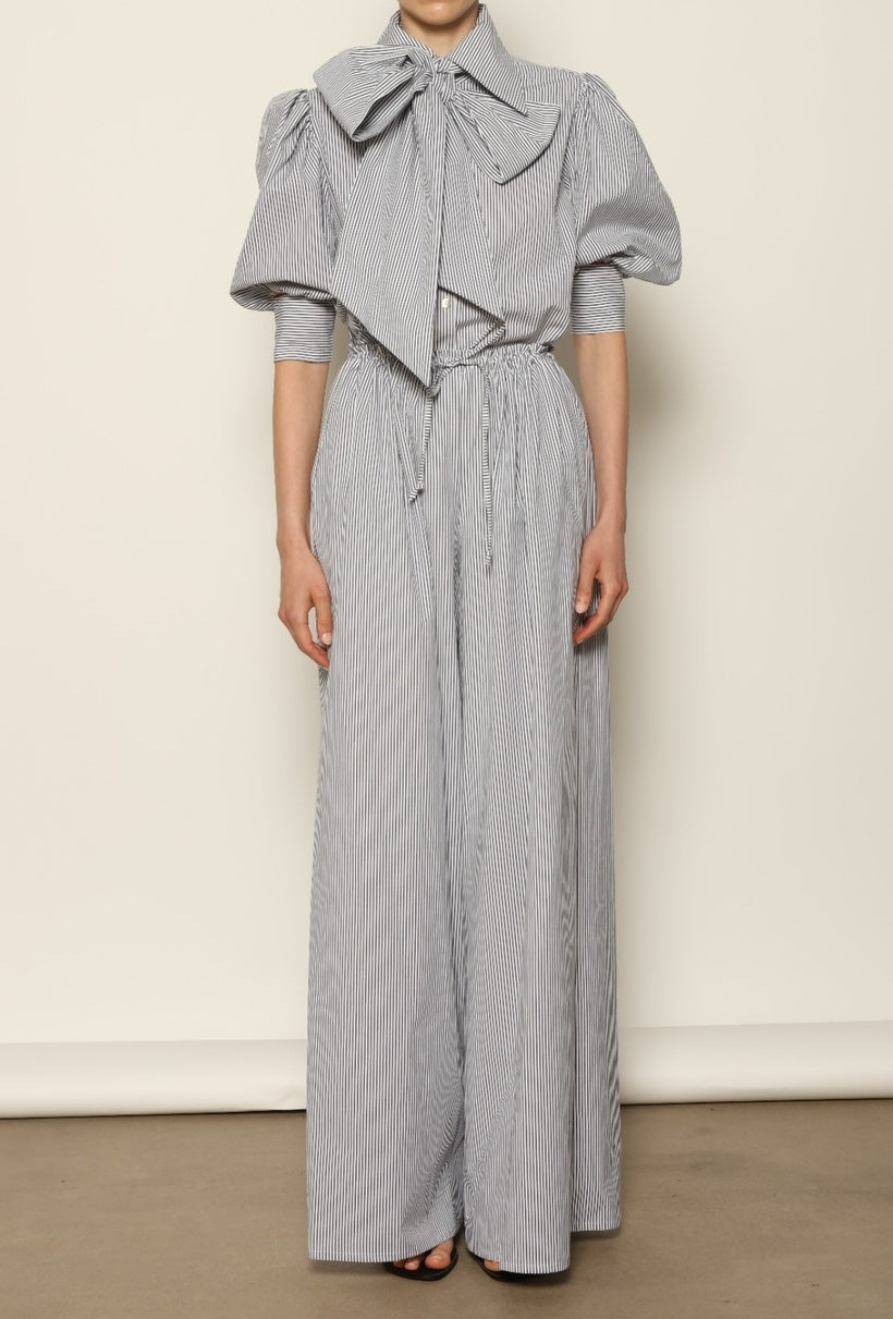 Model wearing the Brigitta White Navy Striped Trousers by House of Woven Stories, featuring 100% organic cotton fabric, high-rise waist, wide-leg silhouette, and classic white and navy stripes.