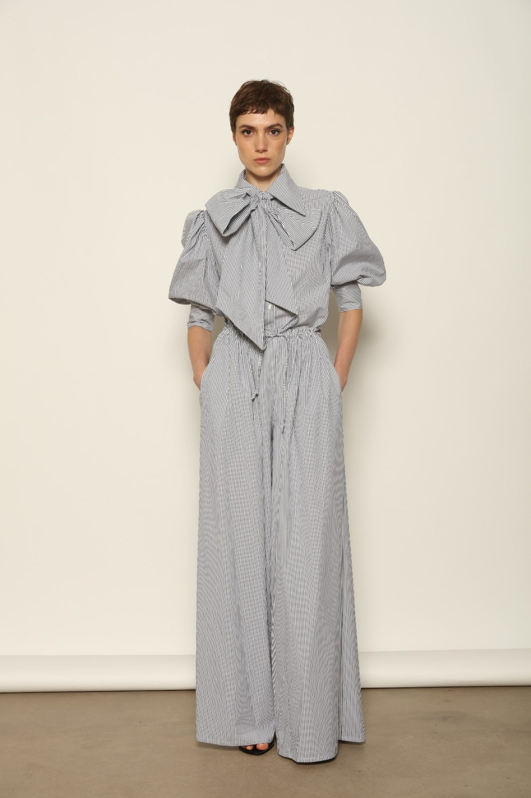 Model wearing the Brigitta White Navy Striped Trousers by House of Woven Stories, featuring 100% organic cotton fabric, high-rise waist, wide-leg silhouette, and classic white and navy stripes.