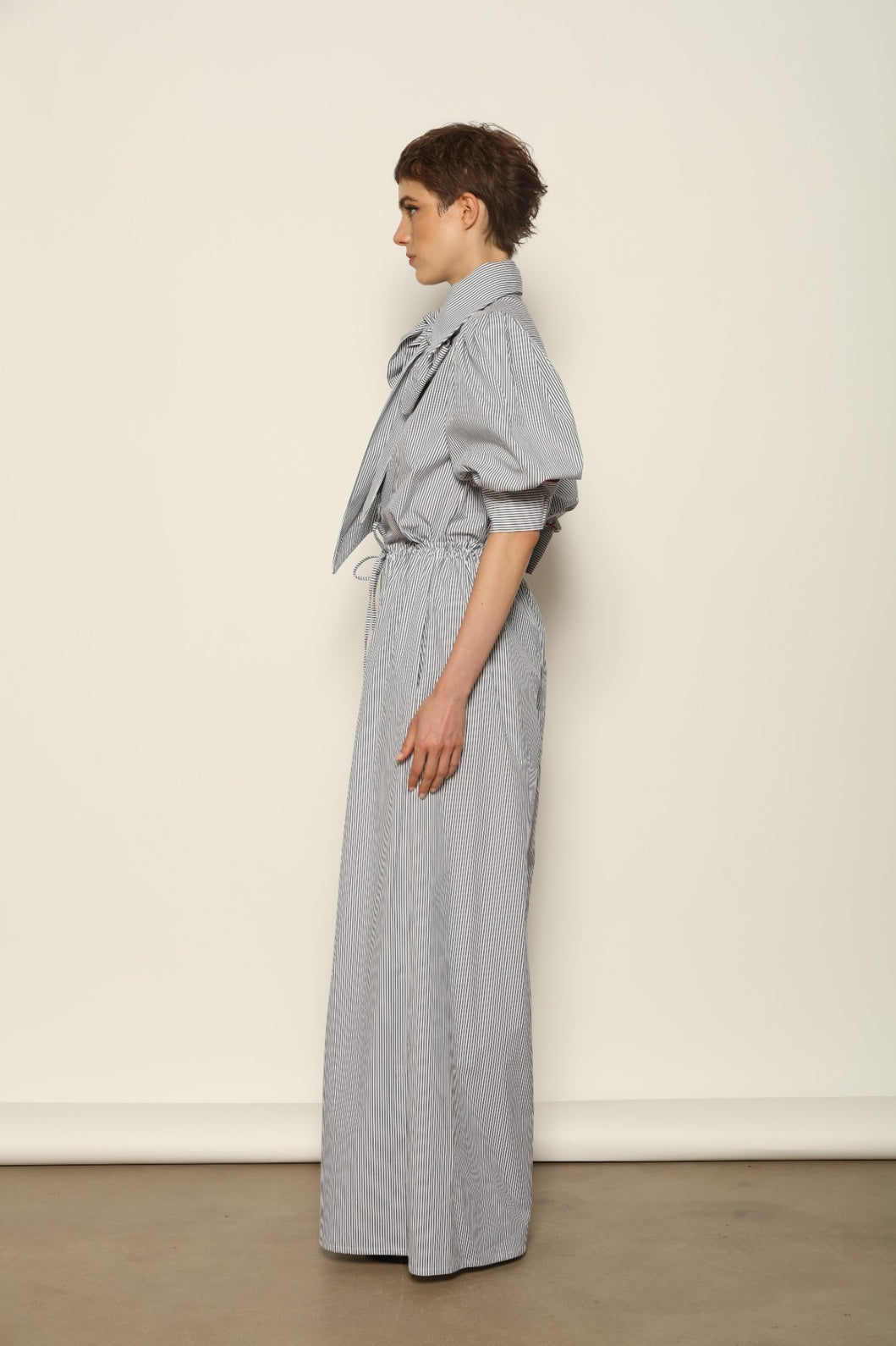 Model wearing the Brigitta White Navy Striped Trousers by House of Woven Stories, featuring 100% organic cotton fabric, high-rise waist, wide-leg silhouette, and classic white and navy stripes.