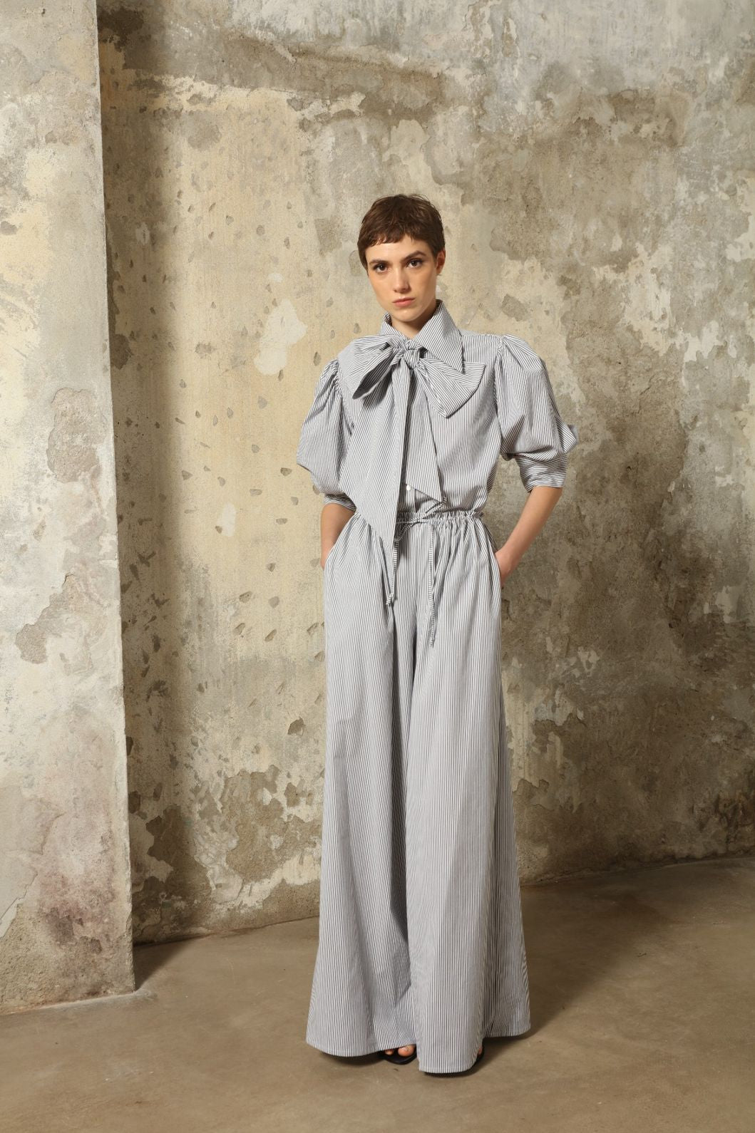 Model wearing the Brigitta White Navy Striped Trousers by House of Woven Stories, featuring 100% organic cotton fabric, high-rise waist, wide-leg silhouette, and classic white and navy stripes.