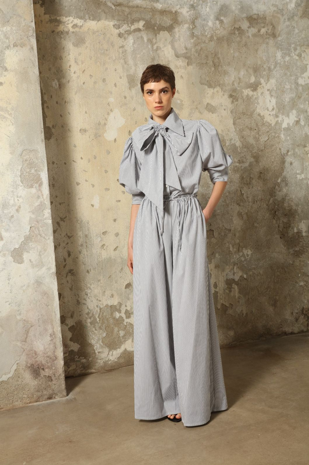 Model wearing the Brigitta White Navy Striped Trousers by House of Woven Stories, featuring 100% organic cotton fabric, high-rise waist, wide-leg silhouette, and classic white and navy stripes.