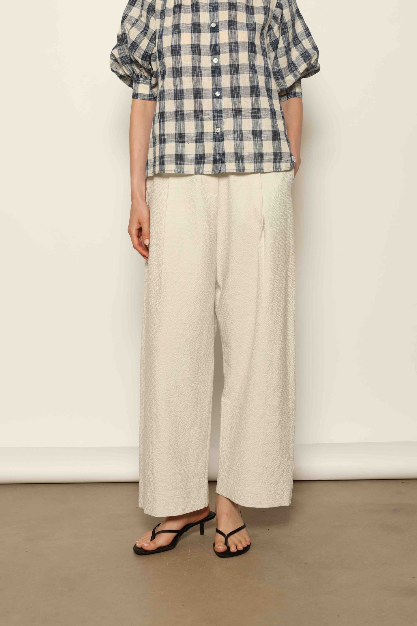 Model wearing the White Brigitta Organic Cotton Trousers by House of Woven Stories, featuring a relaxed fit, lightweight organic cotton fabric, and a timeless minimalist silhouette made in Italy.
