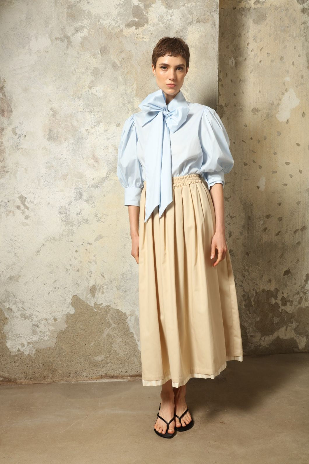 Model wearing the Seoul Camel Skirt by House of Woven Stories, featuring a structured camel-toned fabric, high-waisted fit, and a clean tailored silhouette with defined architectural lines.