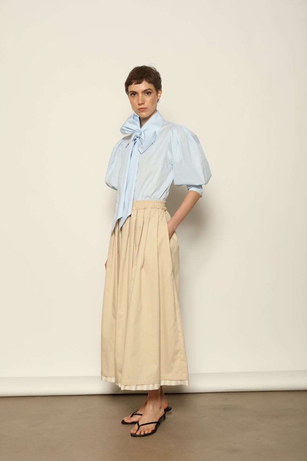 Model wearing the Seoul Camel Skirt by House of Woven Stories, featuring a structured camel-toned fabric, high-waisted fit, and a clean tailored silhouette with defined architectural lines.