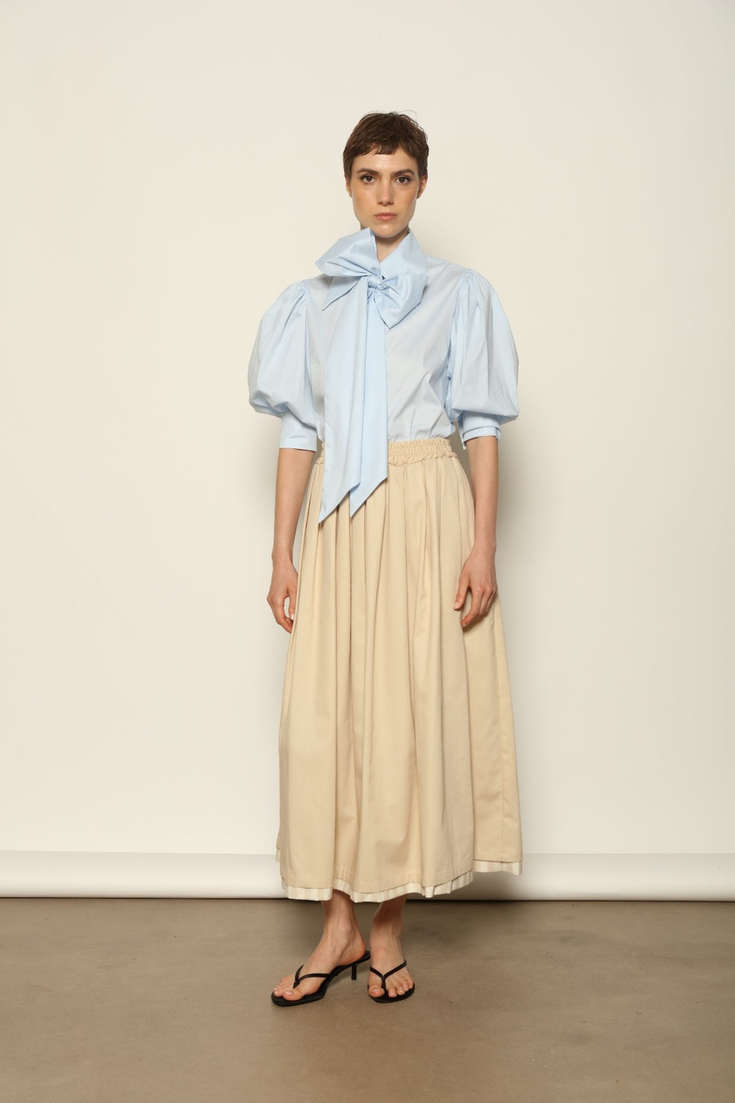 Model wearing the Seoul Camel Skirt by House of Woven Stories, featuring a structured camel-toned fabric, high-waisted fit, and a clean tailored silhouette with defined architectural lines.