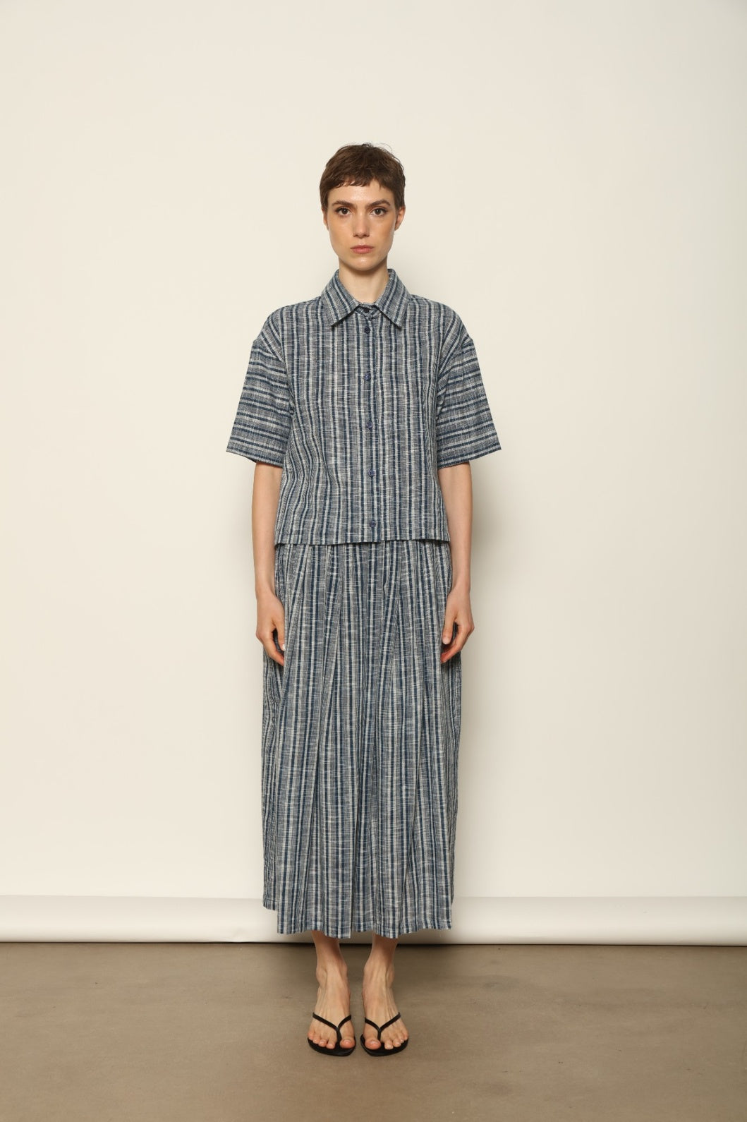 Model wearing the Emily Blue Striped Ikat Shirt by House of Woven Stories, crafted from 100% hand-loomed Kala cotton with indigo stripes, artisanal ikat pattern, and a relaxed cropped silhouette.