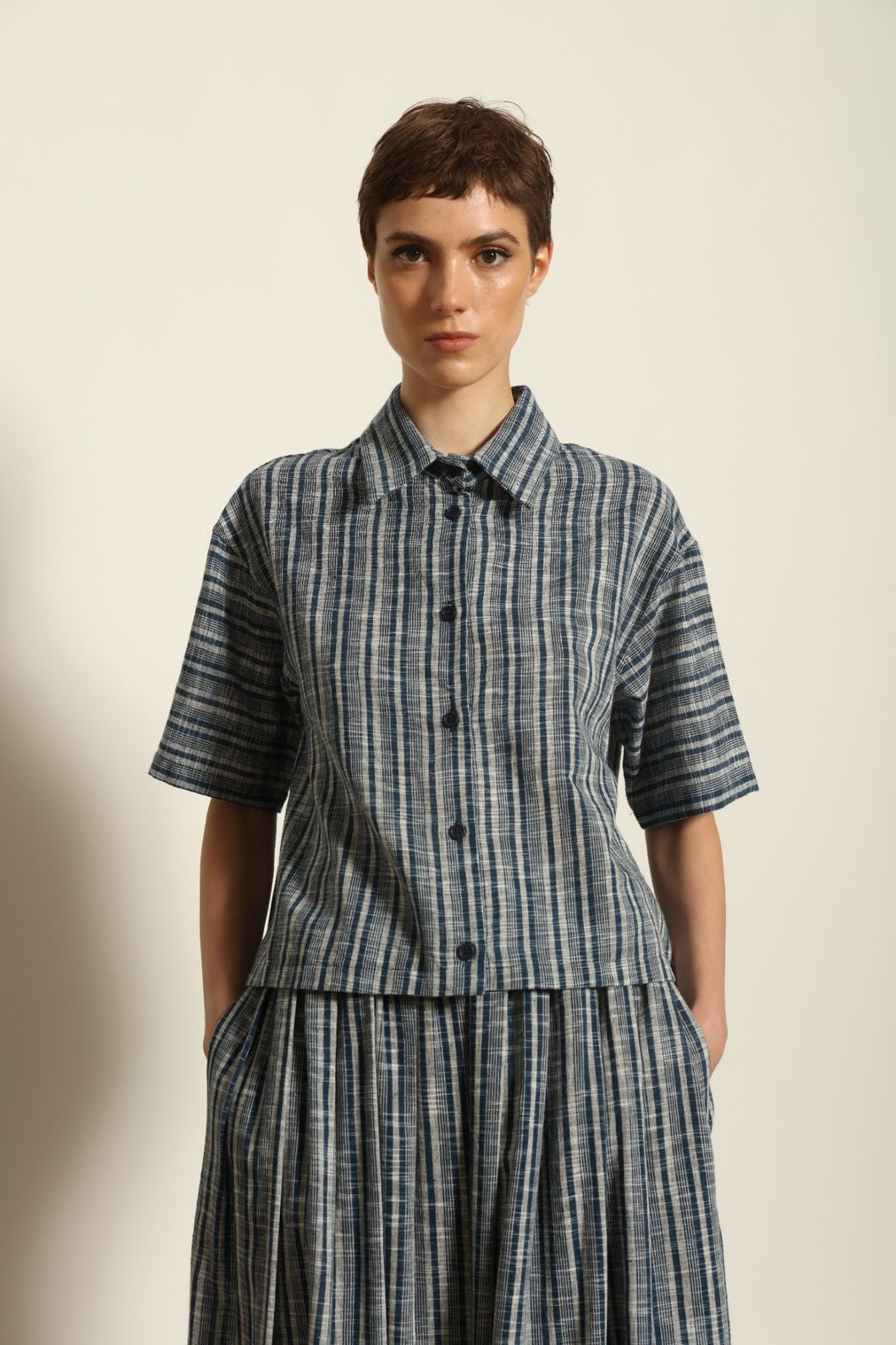 Model wearing the Emily Blue Striped Ikat Shirt by House of Woven Stories, crafted from 100% hand-loomed Kala cotton with indigo stripes, artisanal ikat pattern, and a relaxed cropped silhouette.