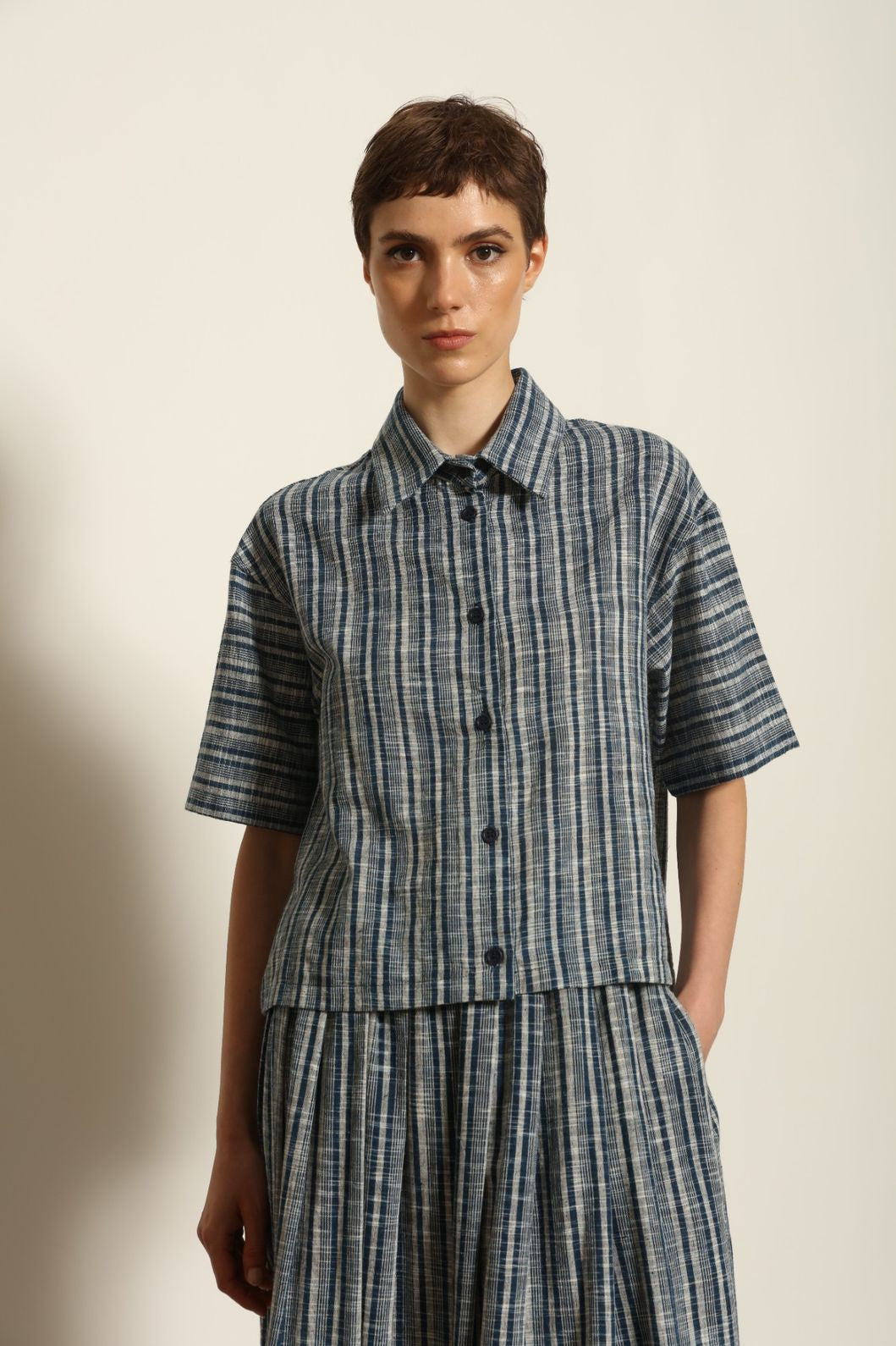 Model wearing the Emily Blue Striped Ikat Shirt by House of Woven Stories, crafted from 100% hand-loomed Kala cotton with indigo stripes, artisanal ikat pattern, and a relaxed cropped silhouette.