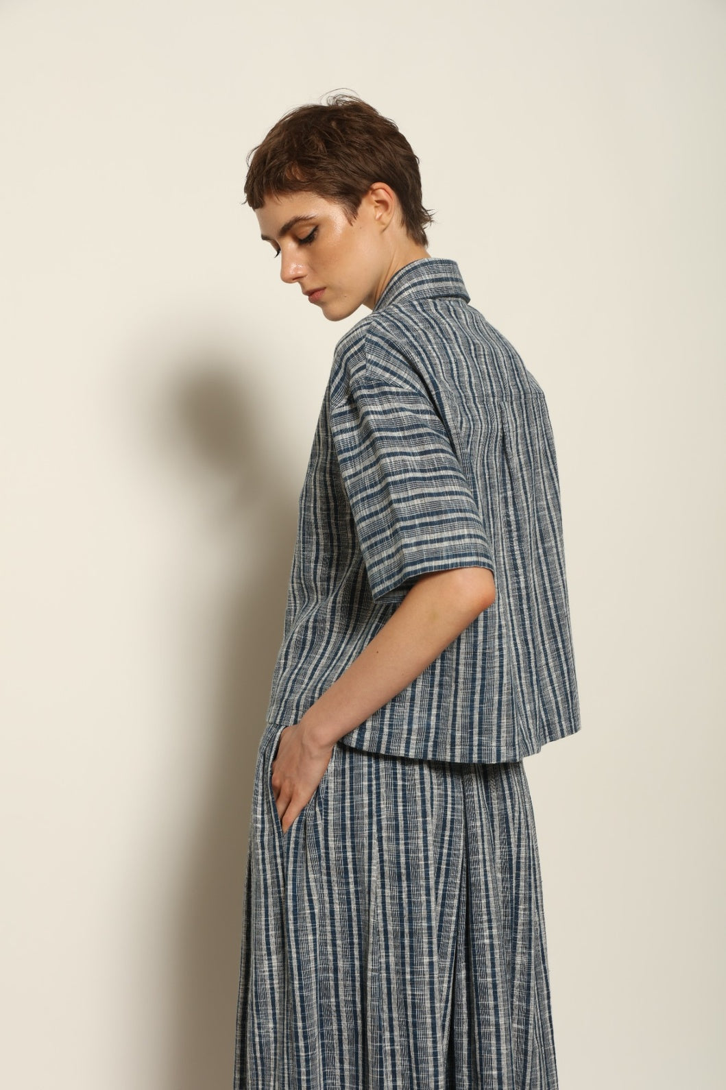 Model wearing the Emily Blue Striped Ikat Shirt by House of Woven Stories, crafted from 100% hand-loomed Kala cotton with indigo stripes, artisanal ikat pattern, and a relaxed cropped silhouette.