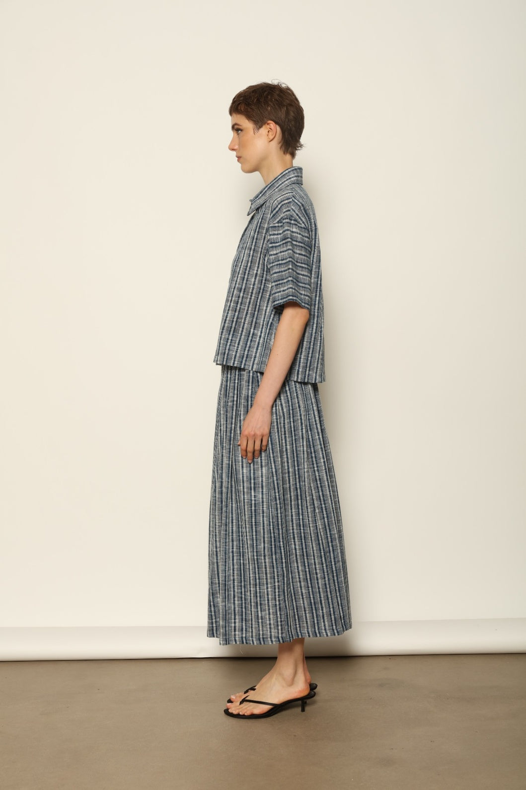 Model wearing the Emily Blue Striped Ikat Shirt by House of Woven Stories, crafted from 100% hand-loomed Kala cotton with indigo stripes, artisanal ikat pattern, and a relaxed cropped silhouette.