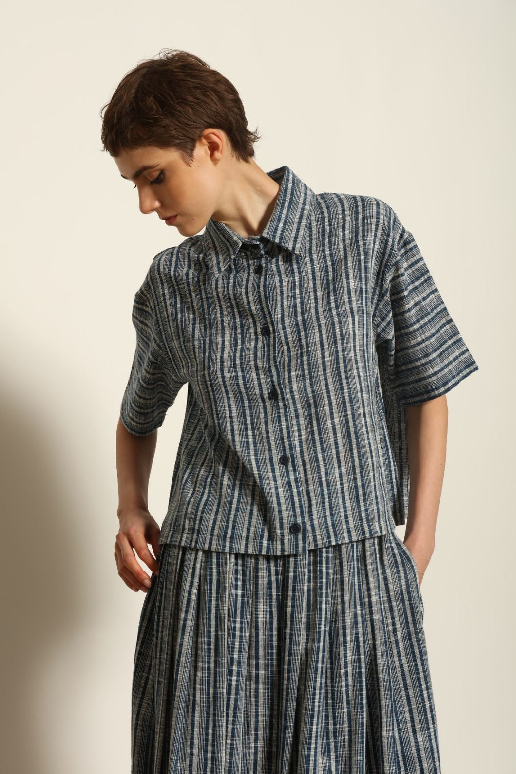 Model wearing the Emily Blue Striped Ikat Shirt by House of Woven Stories, crafted from 100% hand-loomed Kala cotton with indigo stripes, artisanal ikat pattern, and a relaxed cropped silhouette.