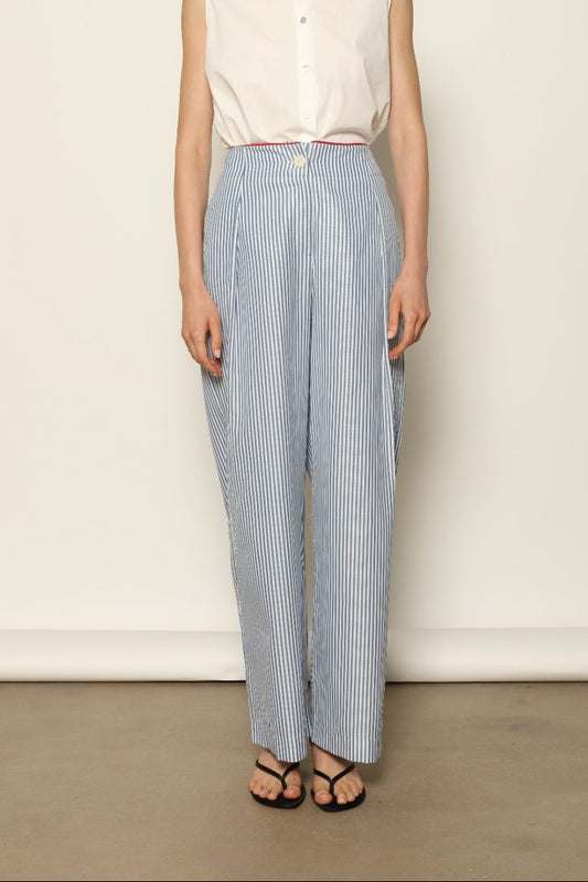Model wearing the Gabriella Blue & White Striped Trousers by House of Woven Stories, featuring 100% cotton fabric, blue and white stripe pattern, relaxed fit, and contrasting red piping at the waistband.