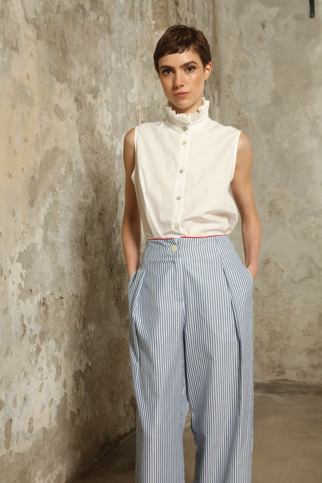 Model wearing the Gabriella Blue & White Striped Trousers by House of Woven Stories, featuring 100% cotton fabric, blue and white stripe pattern, relaxed fit, and contrasting red piping at the waistband.