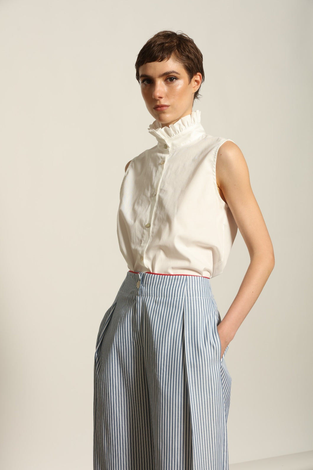 Model wearing the Gabriella Blue & White Striped Trousers by House of Woven Stories, featuring 100% cotton fabric, blue and white stripe pattern, relaxed fit, and contrasting red piping at the waistband.