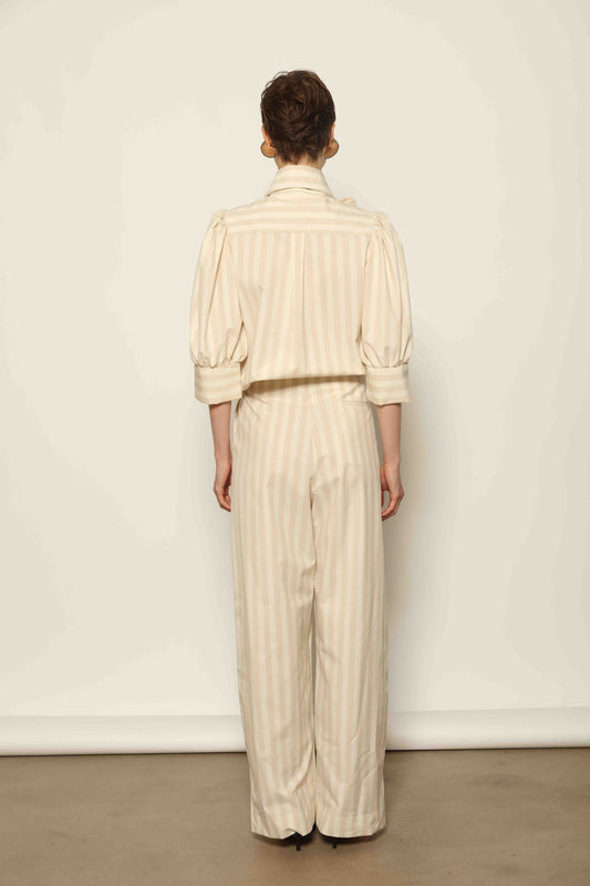 Model wearing the Gabriella Sand White Striped Trousers by House of Woven Stories, featuring a high-rise waist, straight-leg tailored fit, and soft sand and white stripe pattern in a premium cotton, merino wool, and cashmere blend.