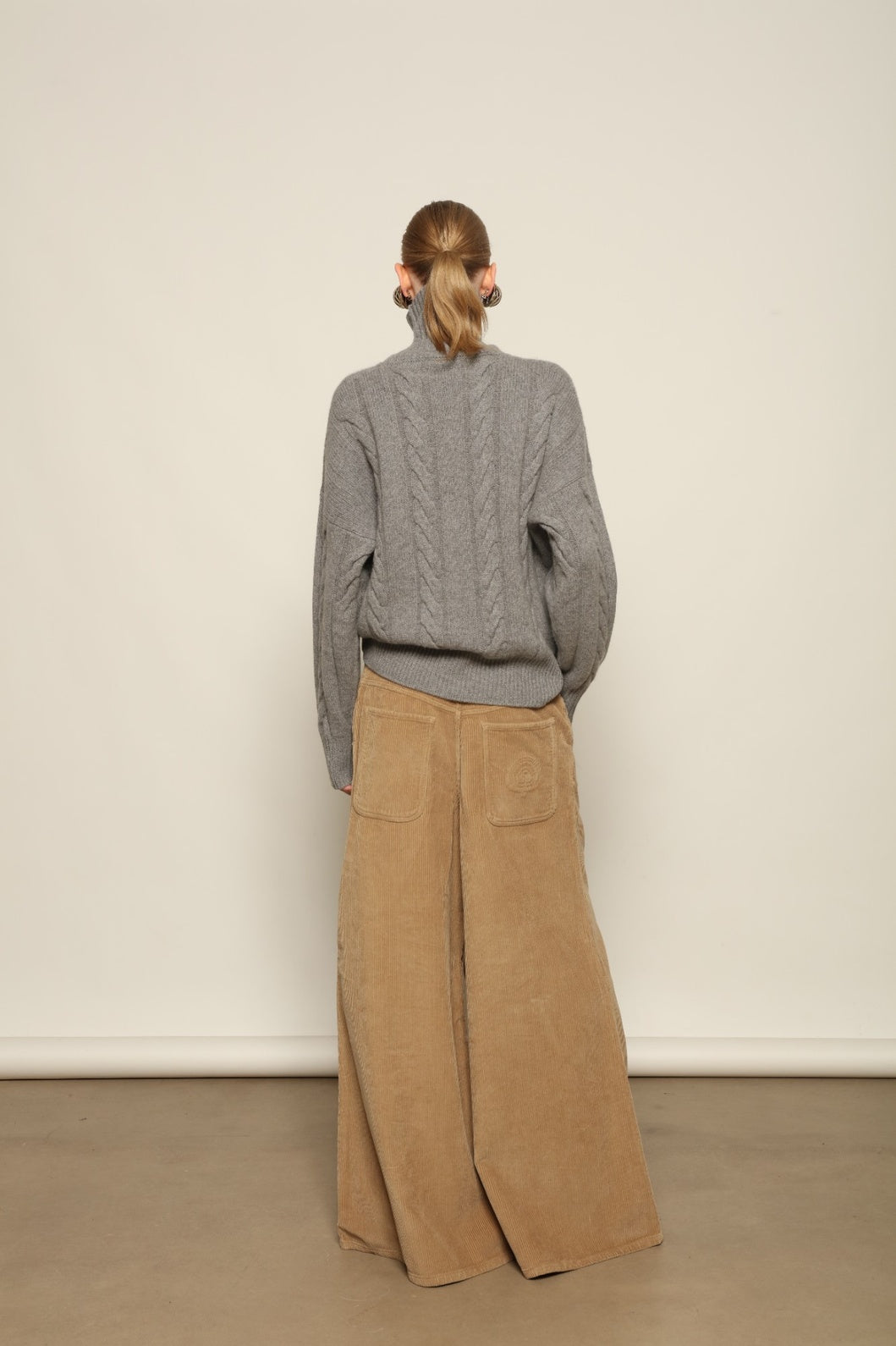 Model is wearing the Graphite Noorah Turtleneck Sweater by House of Woven Stories, a pure ethically sourced cashmere cable-knit sweater with wide ribbed turtleneck and cuffs in graphite.