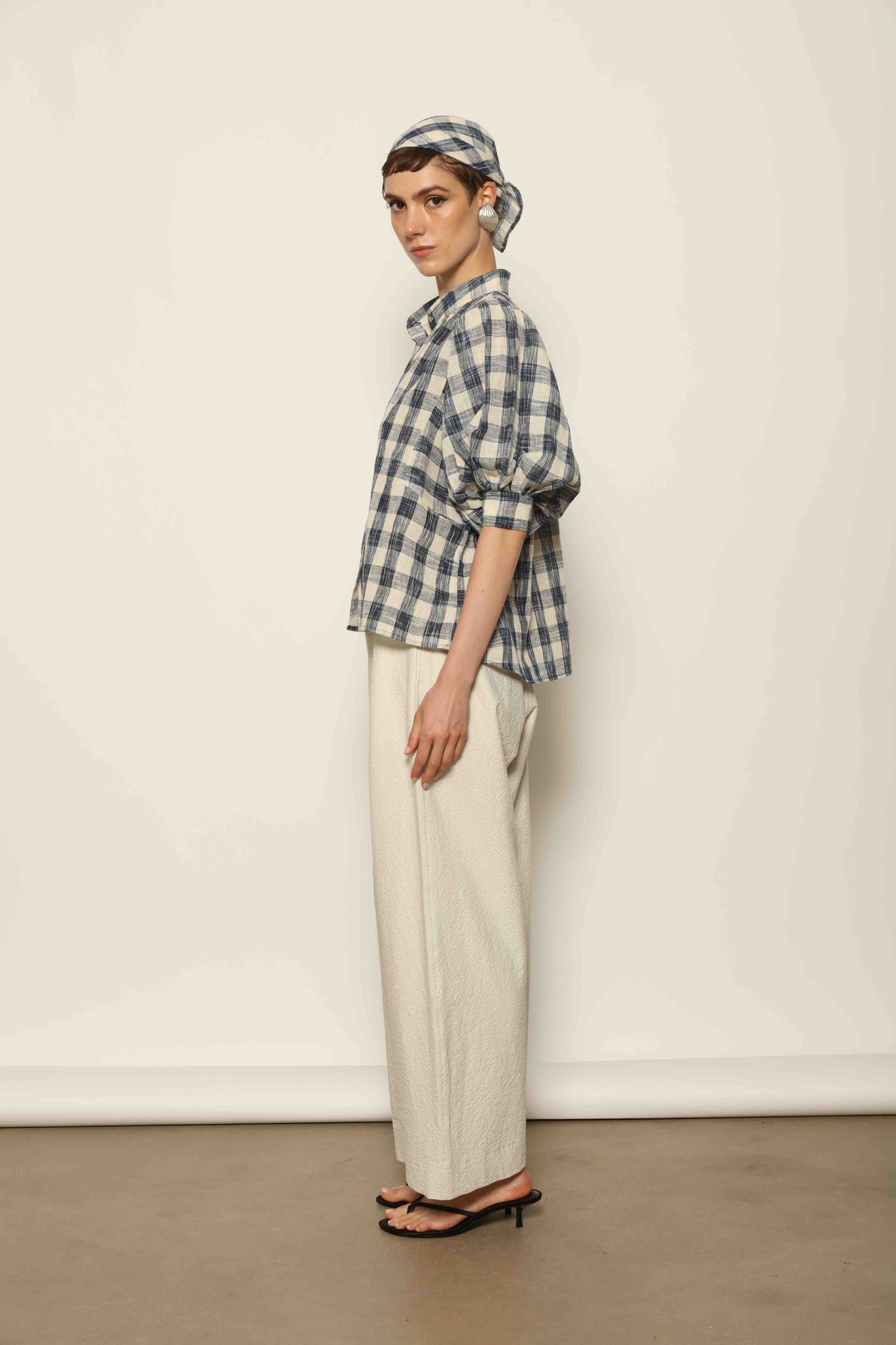 Model wearing the Lola Check Blouse by House of Woven Stories, crafted from 100% handloomed Kala cotton with a blue and white check pattern, Mandarin collar, button-front closure, and balloon sleeves.