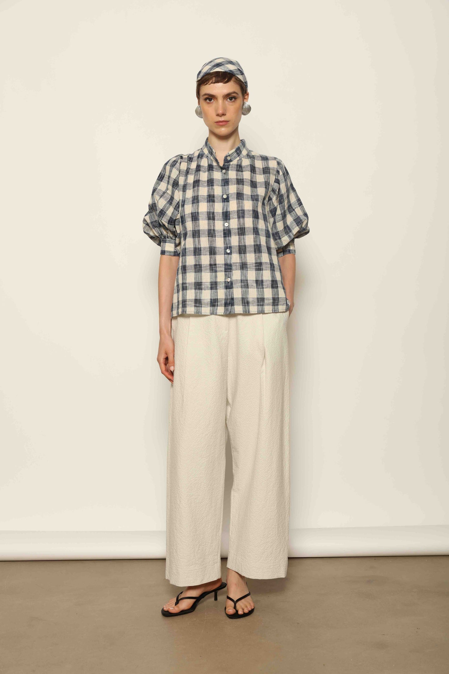 Model wearing the Lola Check Blouse by House of Woven Stories, crafted from 100% handloomed Kala cotton with a blue and white check pattern, Mandarin collar, button-front closure, and balloon sleeves.