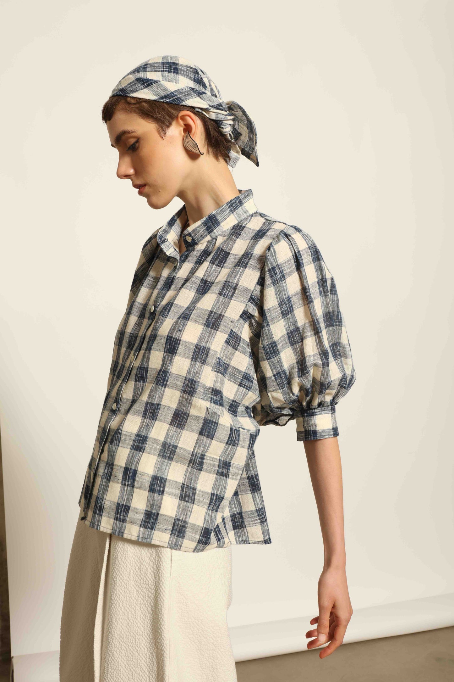 Model wearing the Lola Check Blouse by House of Woven Stories, crafted from 100% handloomed Kala cotton with a blue and white check pattern, Mandarin collar, button-front closure, and balloon sleeves.