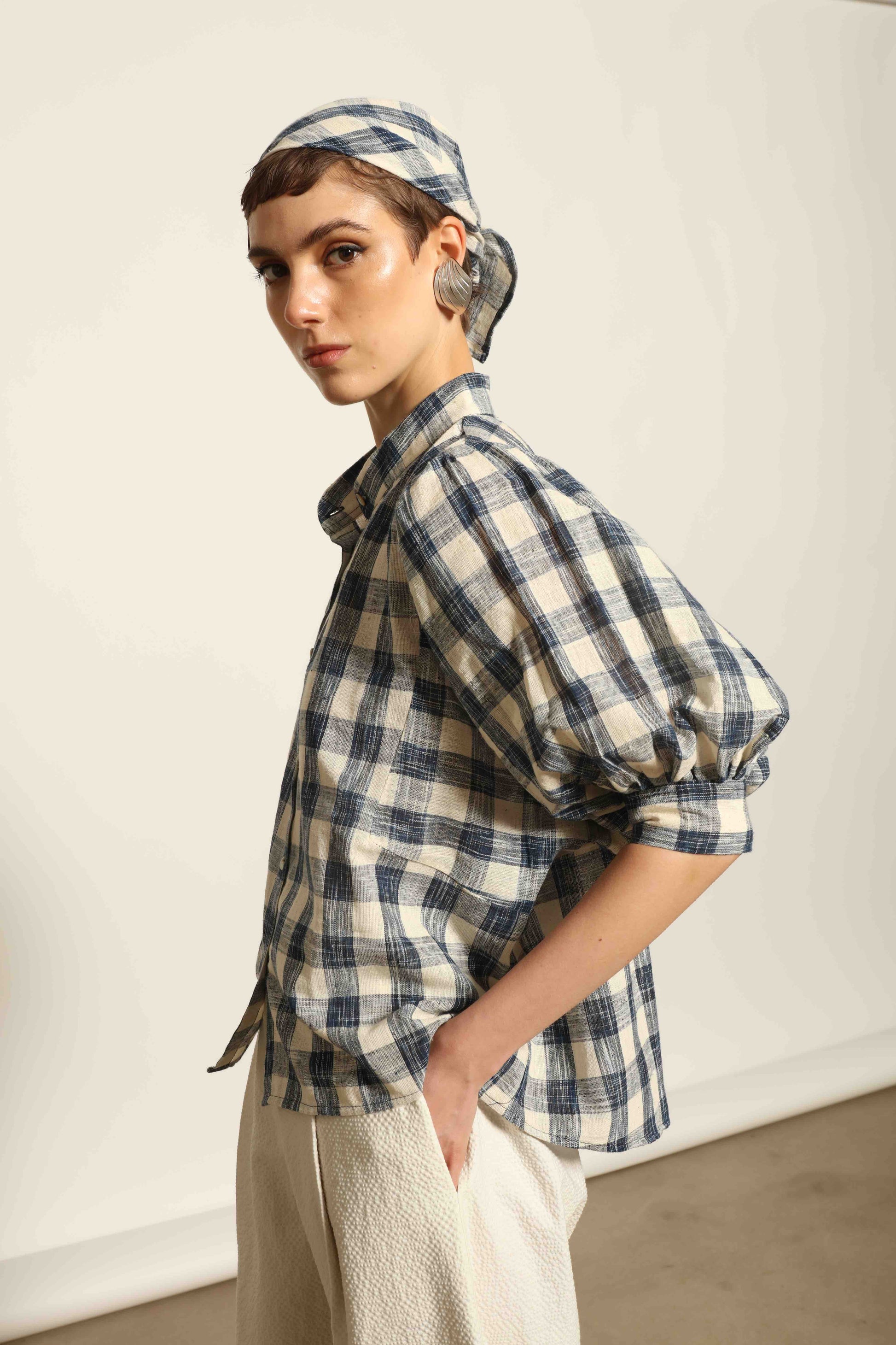 Model wearing the Lola Check Blouse by House of Woven Stories, crafted from 100% handloomed Kala cotton with a blue and white check pattern, Mandarin collar, button-front closure, and balloon sleeves.