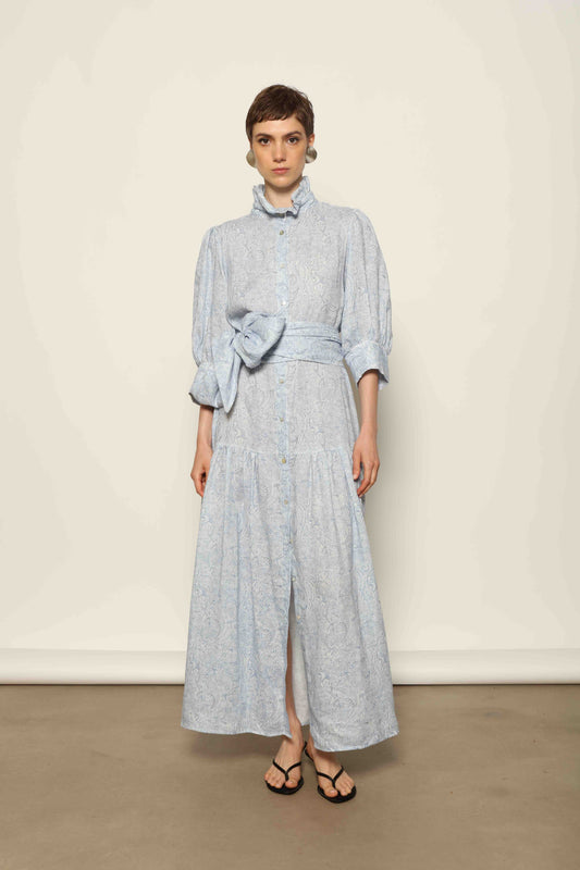 Model wearing the Karin Blue Paisley Dress by House of Woven Stories, featuring 100% linen fabric, soft blue paisley print, and a relaxed flowing silhouette with breathable lightweight structure.