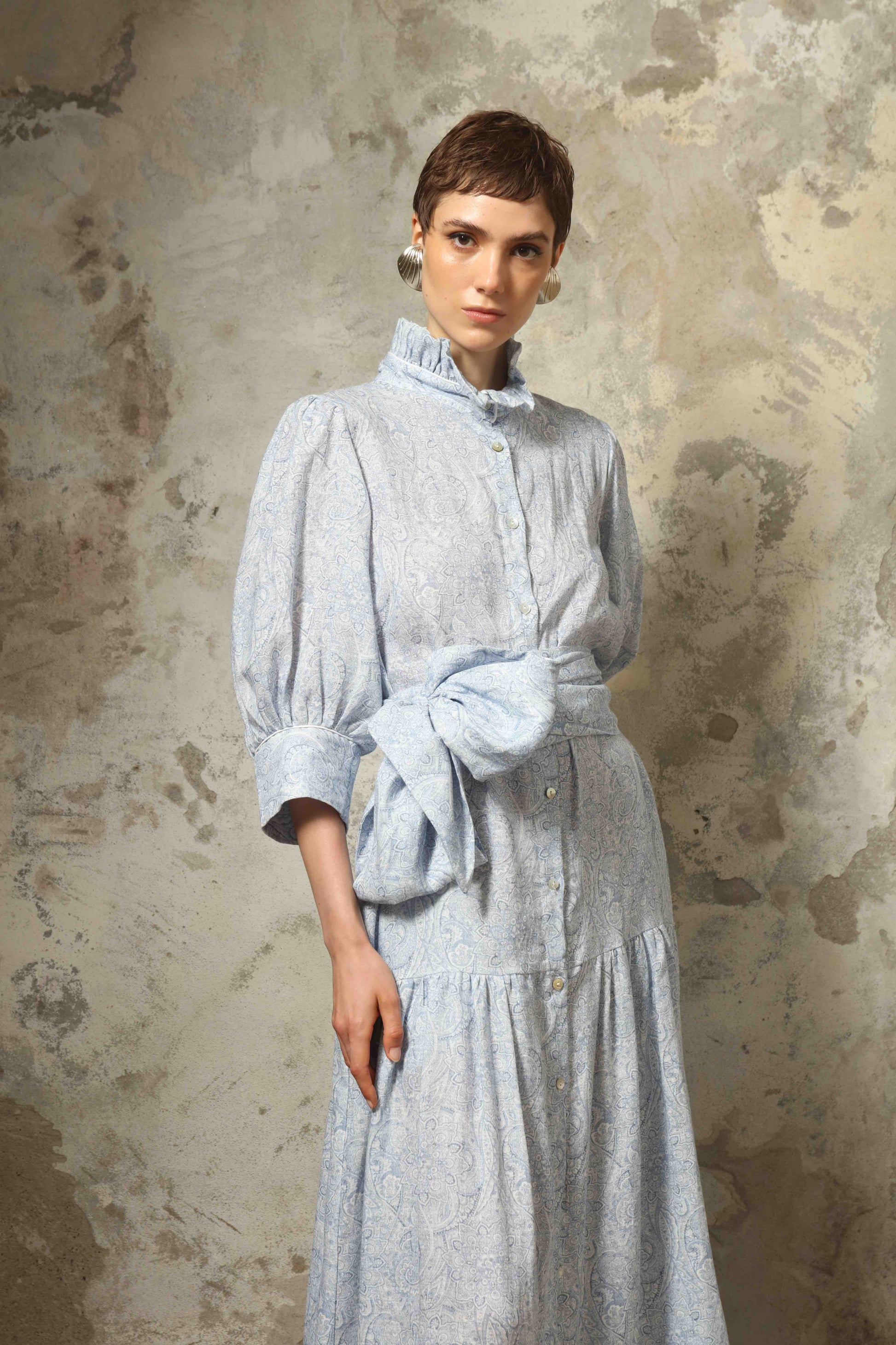 Model wearing the Karin Blue Paisley Dress by House of Woven Stories, featuring 100% linen fabric, soft blue paisley print, and a relaxed flowing silhouette with breathable lightweight structure.