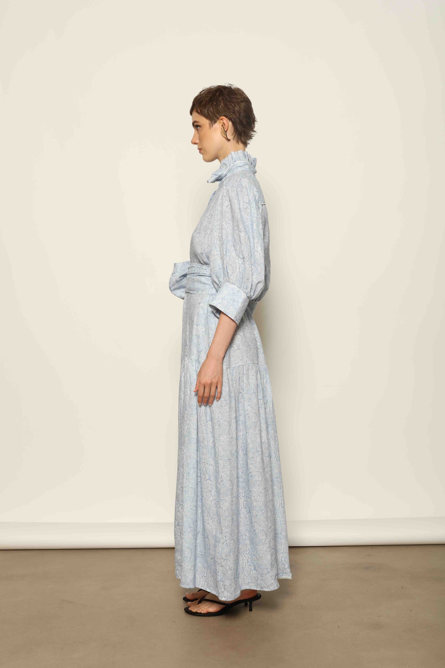 Model wearing the Karin Blue Paisley Dress by House of Woven Stories, featuring 100% linen fabric, soft blue paisley print, and a relaxed flowing silhouette with breathable lightweight structure.