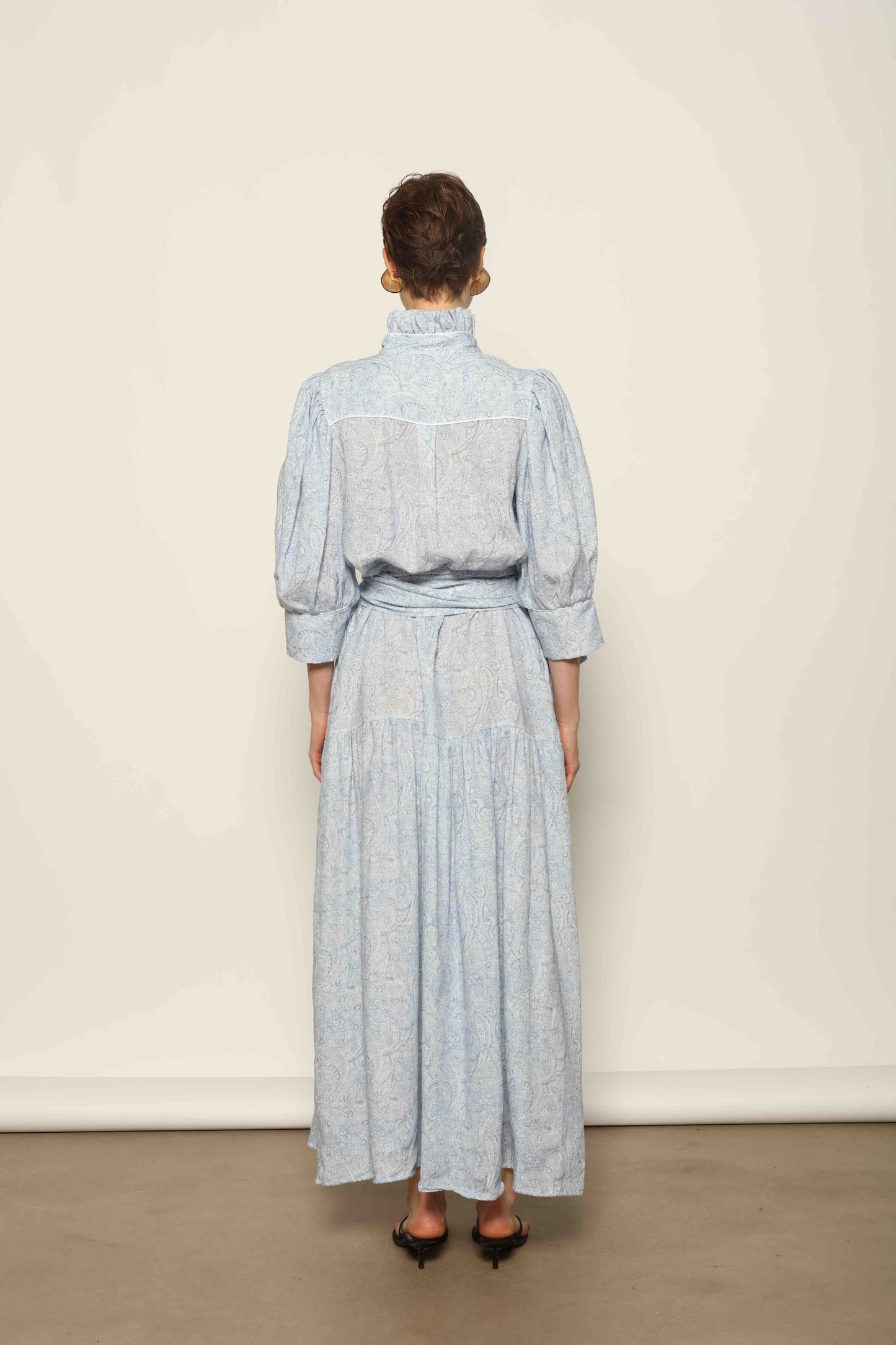 Model wearing the Karin Blue Paisley Dress by House of Woven Stories, featuring 100% linen fabric, soft blue paisley print, and a relaxed flowing silhouette with breathable lightweight structure.