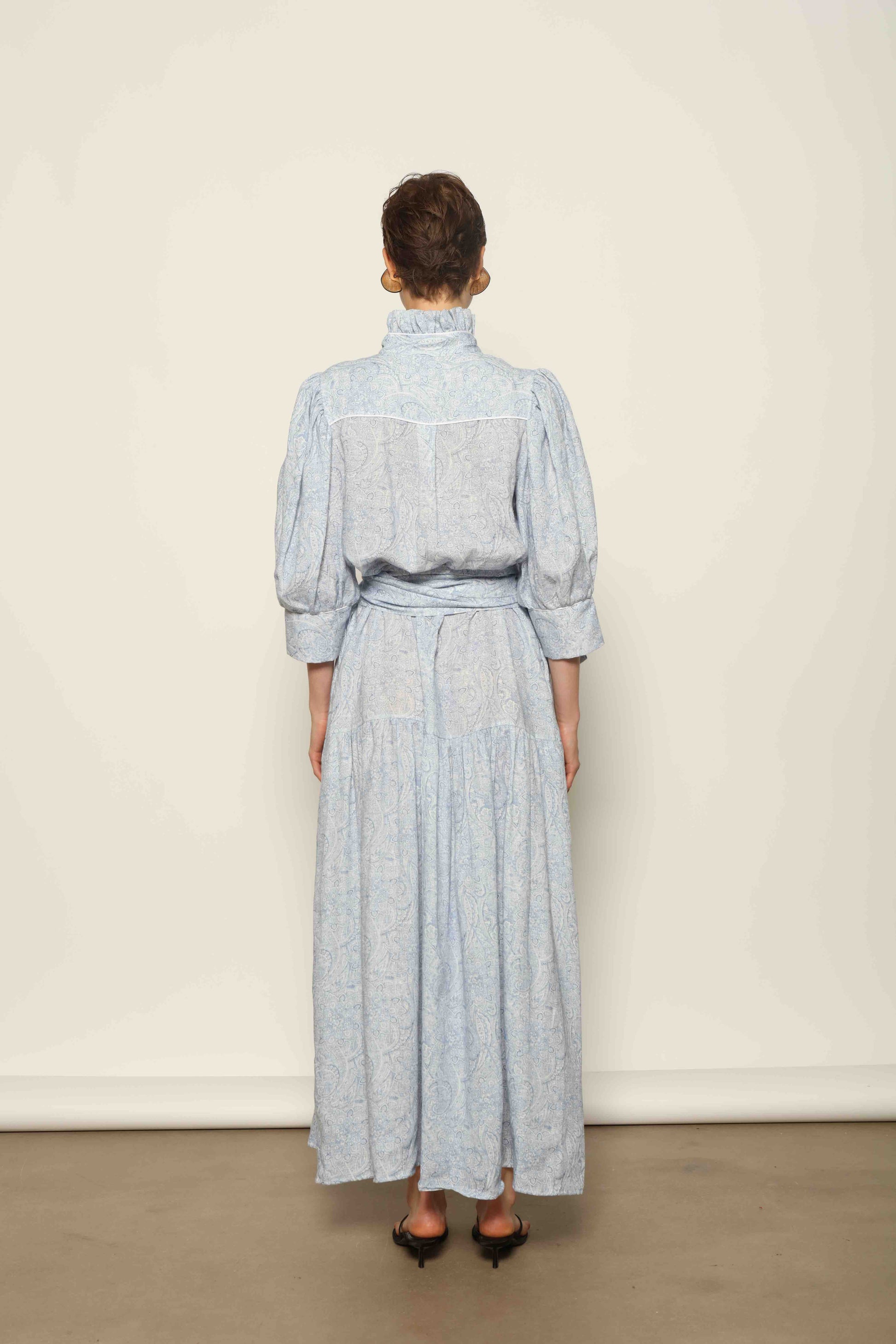 Model wearing the Karin Blue Paisley Dress by House of Woven Stories, featuring 100% linen fabric, soft blue paisley print, and a relaxed flowing silhouette with breathable lightweight structure.