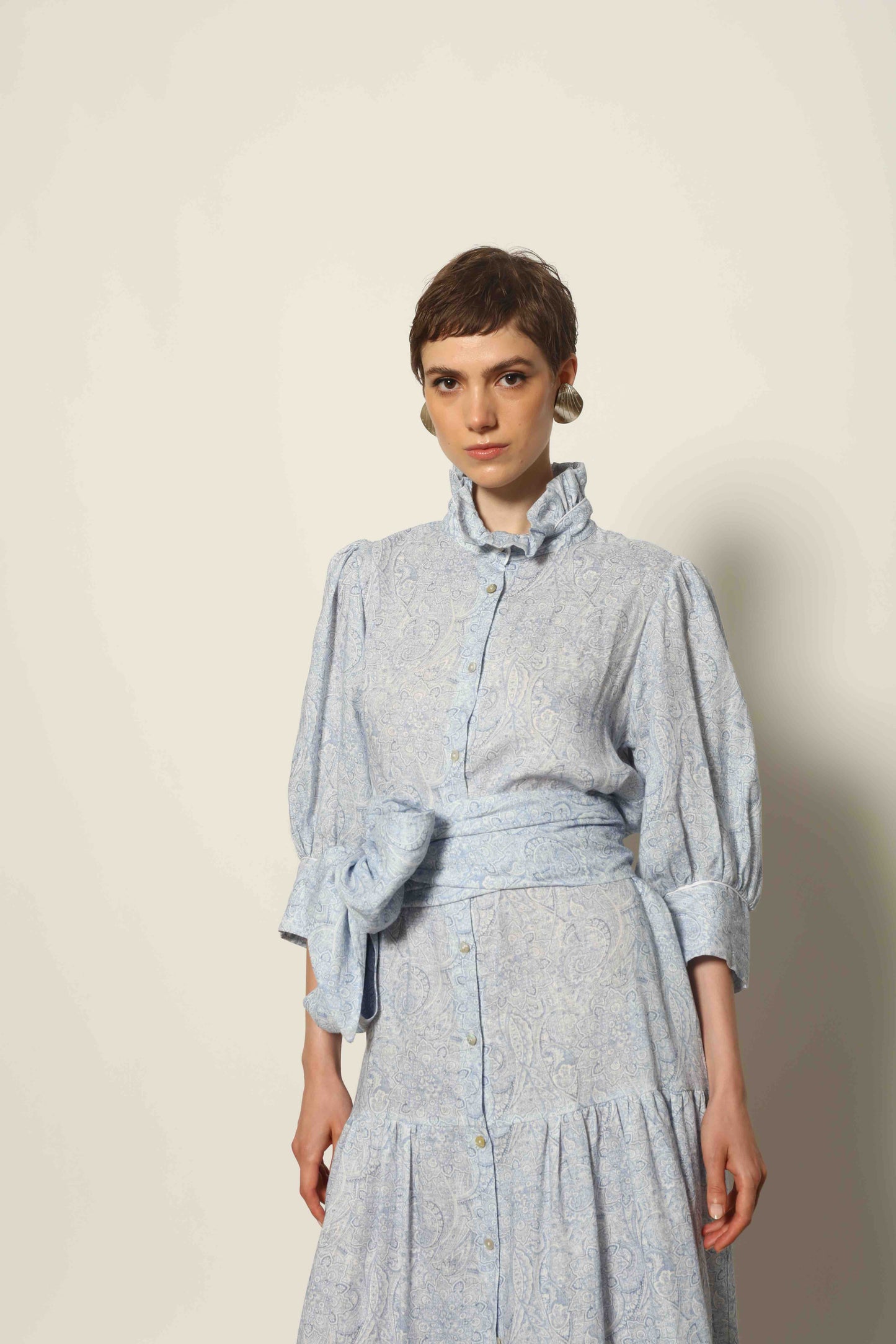 Model wearing the Karin Blue Paisley Dress by House of Woven Stories, featuring 100% linen fabric, soft blue paisley print, and a relaxed flowing silhouette with breathable lightweight structure.