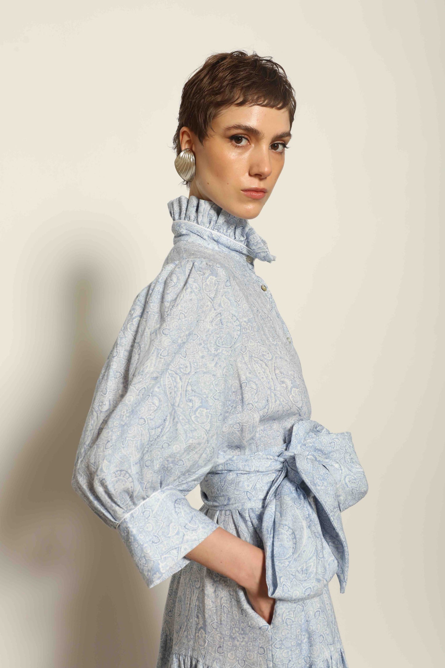 Model wearing the Karin Blue Paisley Dress by House of Woven Stories, featuring 100% linen fabric, soft blue paisley print, and a relaxed flowing silhouette with breathable lightweight structure.
