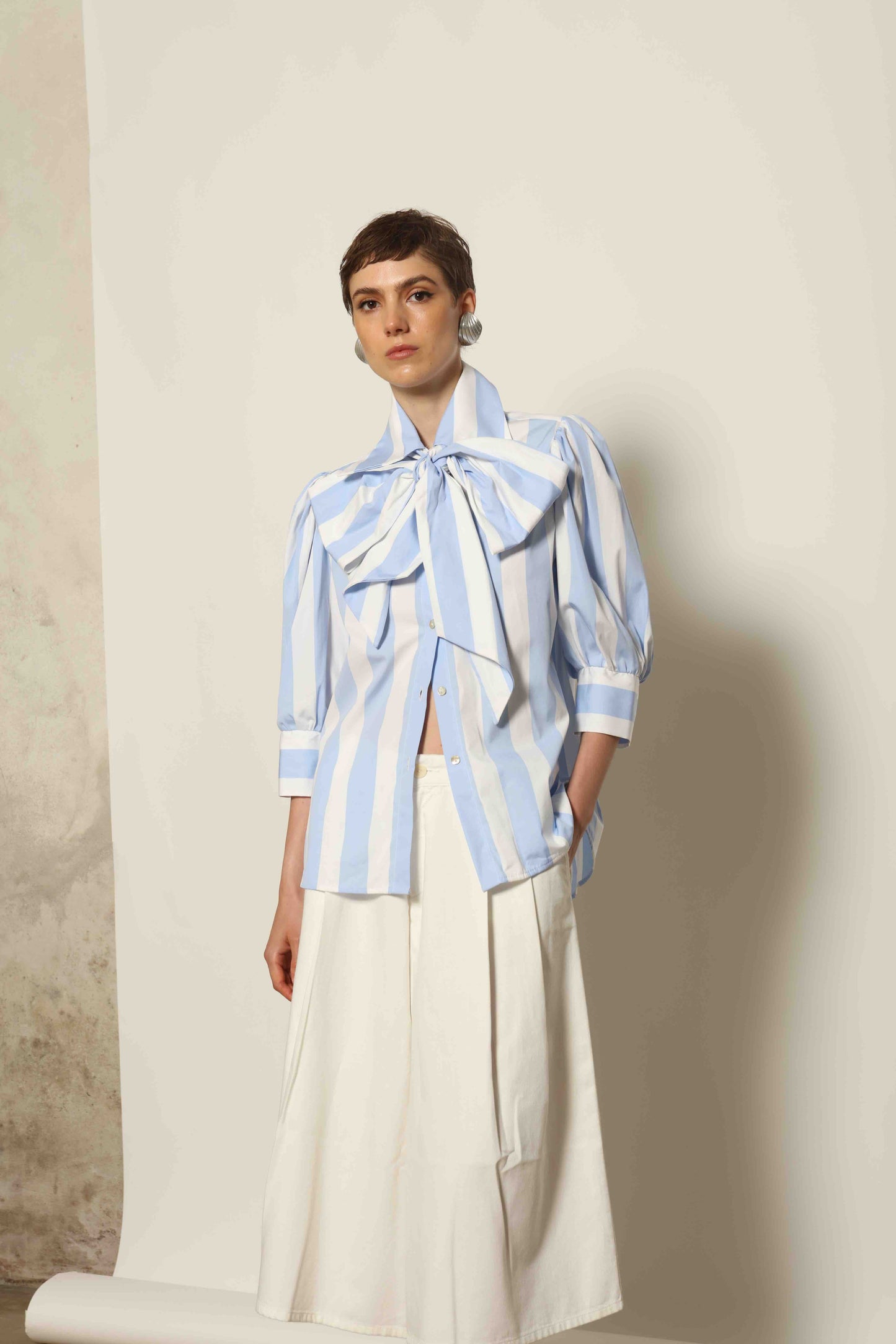 Model wearing the Karin Blue and White Macro Striped Blouse by House of Woven Stories, featuring bold macro stripes, relaxed fit silhouette, and lightweight 100% organic cotton fabric made in Italy.