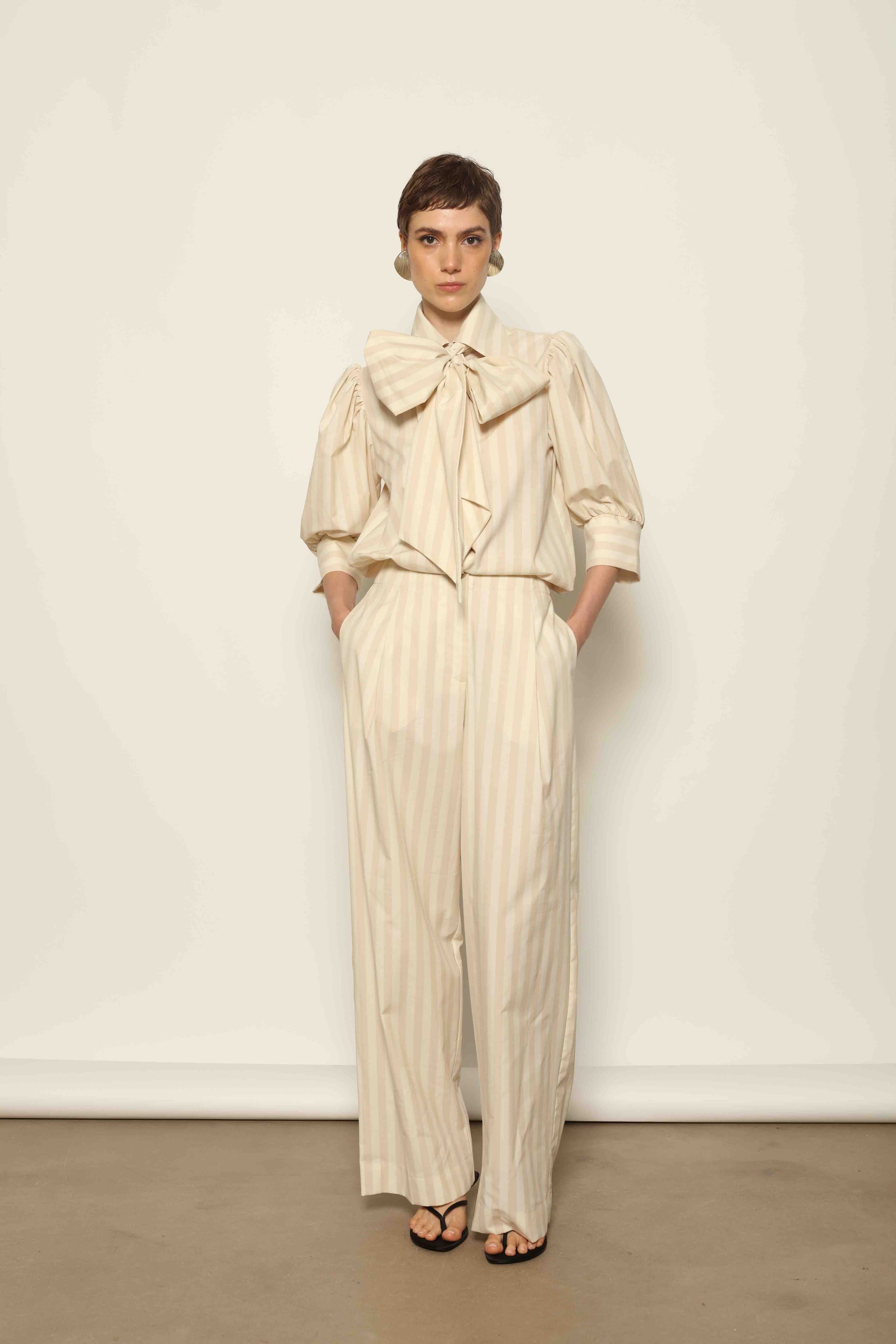 Model wearing the Karin Sand White Macro-Striped Blouse by House of Nomad Stories, featuring a relaxed fit, sand and white macro stripes, classic collar, and soft blend of cotton, merino wool, and cashmere.