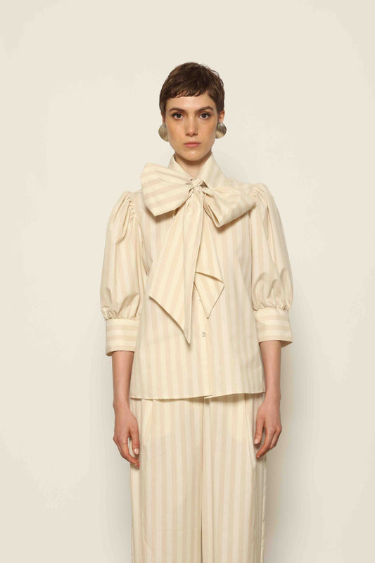 Model wearing the Karin Sand White Macro-Striped Blouse by House of Nomad Stories, featuring a relaxed fit, sand and white macro stripes, classic collar, and soft blend of cotton, merino wool, and cashmere.