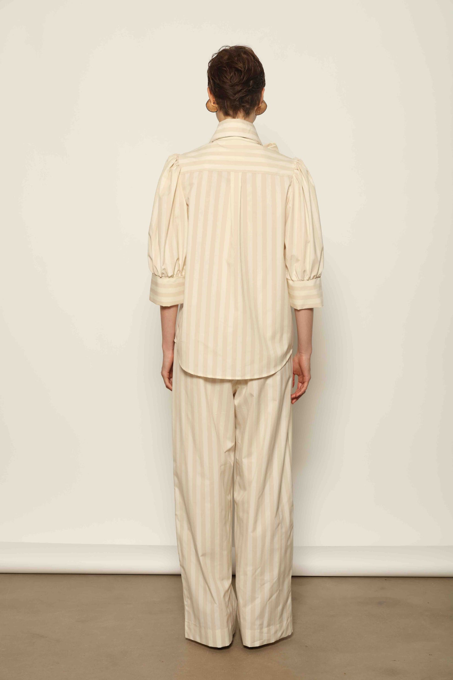Model wearing the Karin Sand White Macro-Striped Blouse by House of Nomad Stories, featuring a relaxed fit, sand and white macro stripes, classic collar, and soft blend of cotton, merino wool, and cashmere.