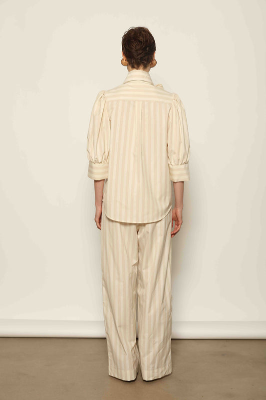 Model wearing the Karin Sand White Macro-Striped Blouse by House of Nomad Stories, featuring a relaxed fit, sand and white macro stripes, classic collar, and soft blend of cotton, merino wool, and cashmere.
