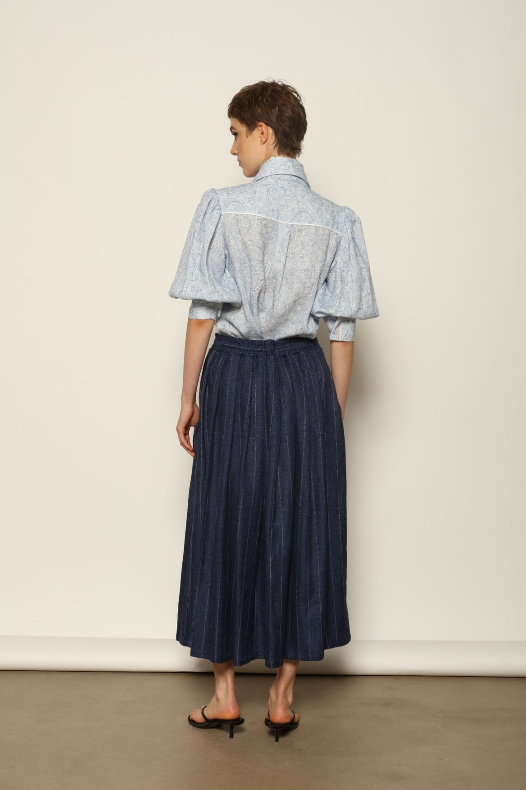 Model wearing the Karin White Blue Paisley Blouse by House of Nomad Stories, featuring 100% linen fabric, blue and white paisley print, relaxed short sleeves, and a classic collar with tie detail.