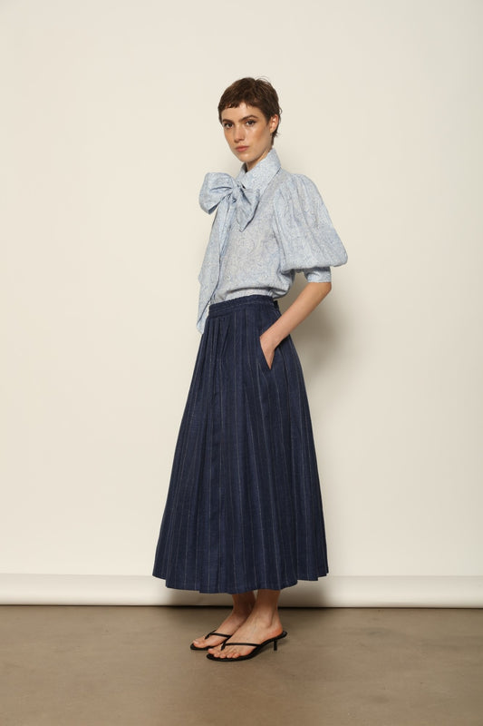Model wearing the Karin White Blue Paisley Blouse by House of Nomad Stories, featuring 100% linen fabric, blue and white paisley print, relaxed short sleeves, and a classic collar with tie detail.