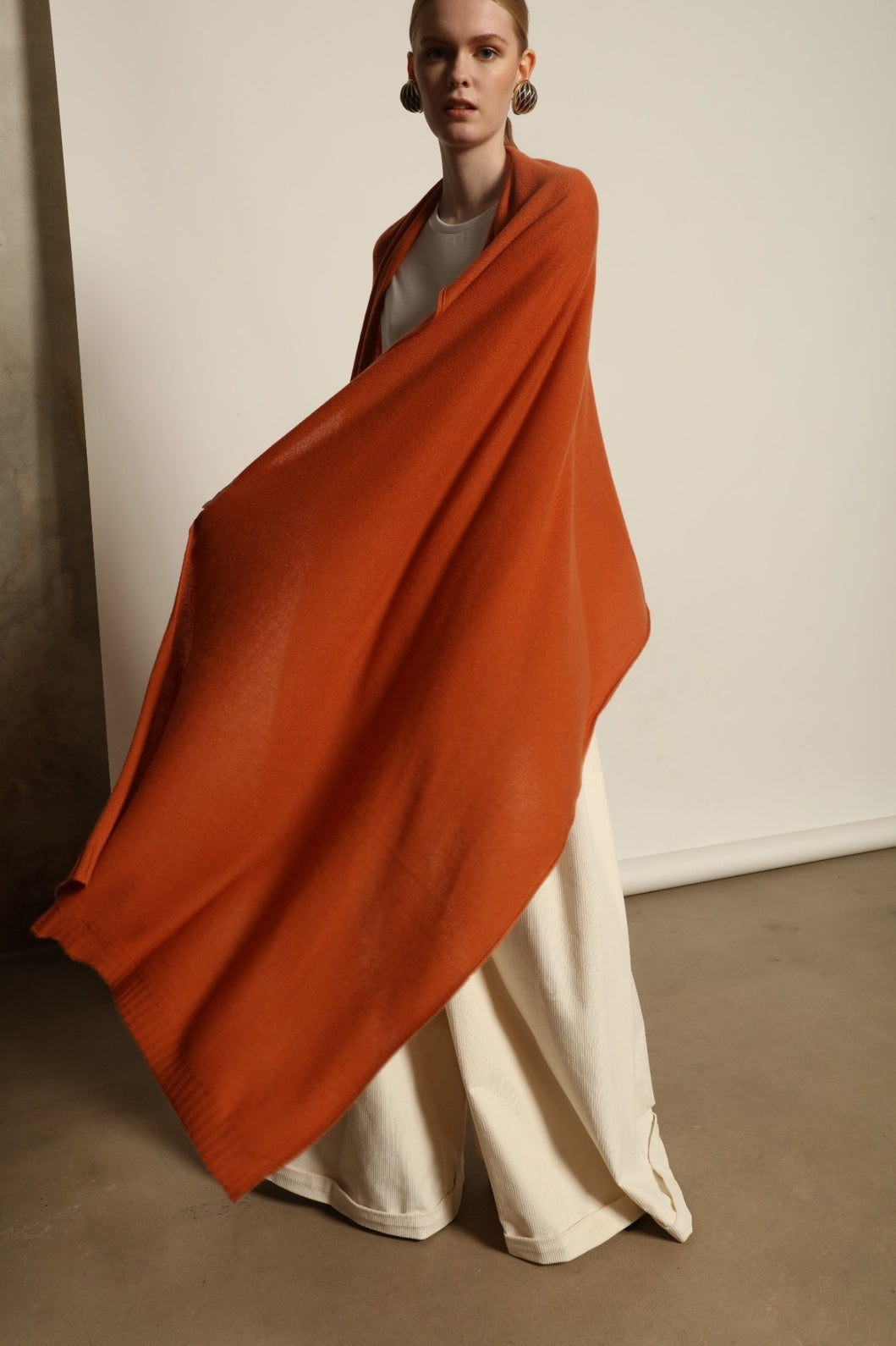 Model is wearing the Brick Leni Scarf by House of Woven Stories, a pure ethically sourced cashmere scarf with refined texture, enduring softness and fluid drape in a warm brick tone.