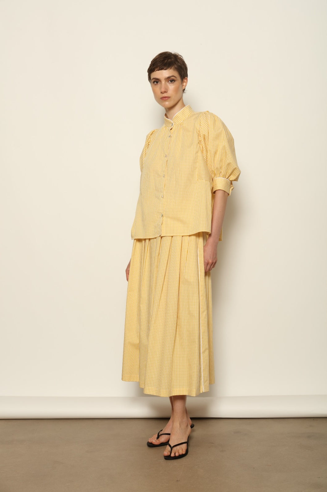 Model wearing the Lola Vichy Butter Yellow Blouse by House of Woven Stories, featuring 100% organic cotton fabric, butter yellow gingham check, short balloon sleeves, and contrasting white piping details.